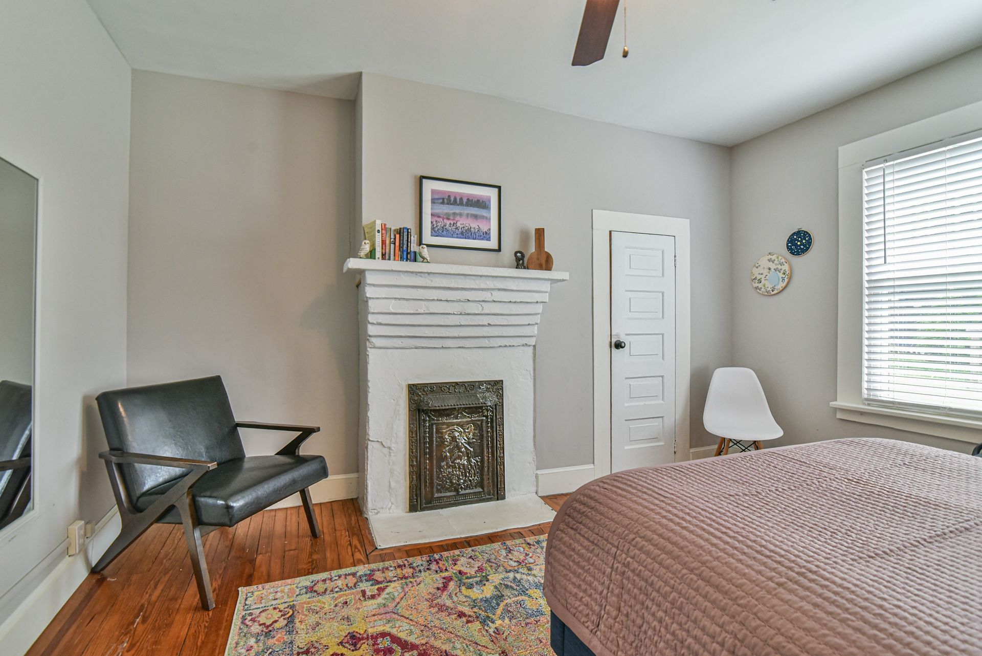 Bedroom with a fireplace, black chair, bed, white walls, and a window with blinds