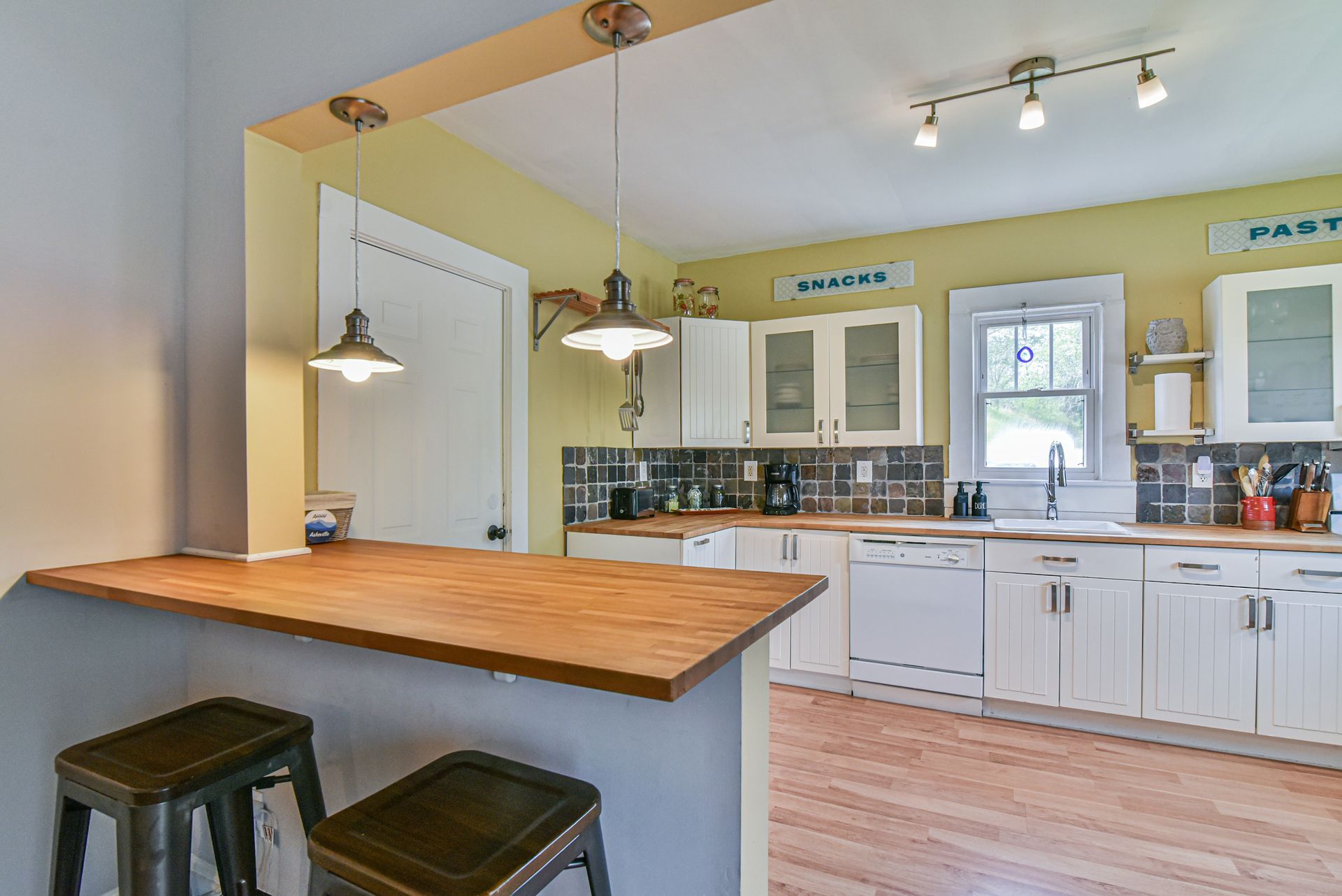 Bright kitchen with white cabinets, wood countertops, island bar, and pendant lighting