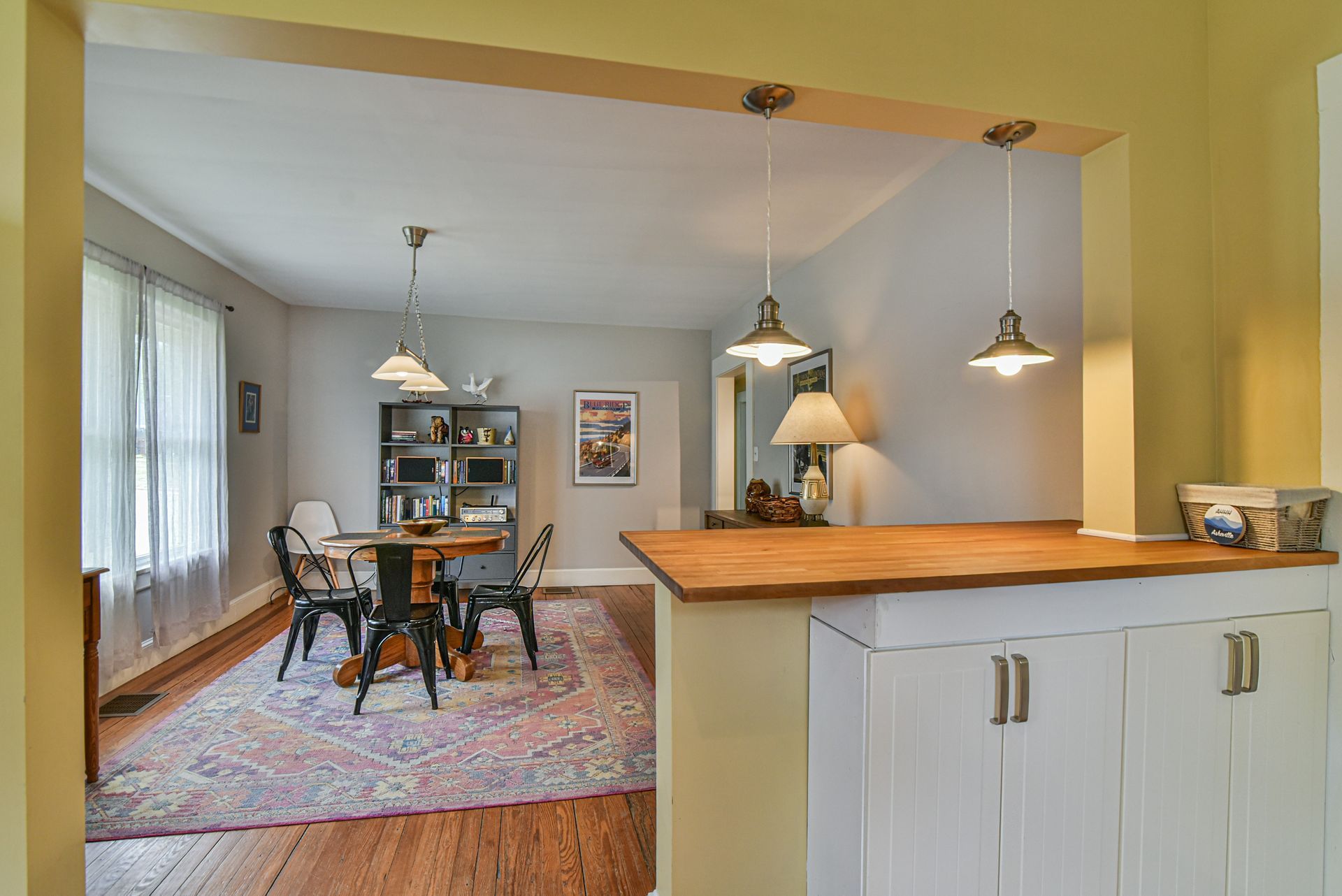 Open-plan dining area with wooden table, pendant lights, rug, and pass-through counter to kitchen