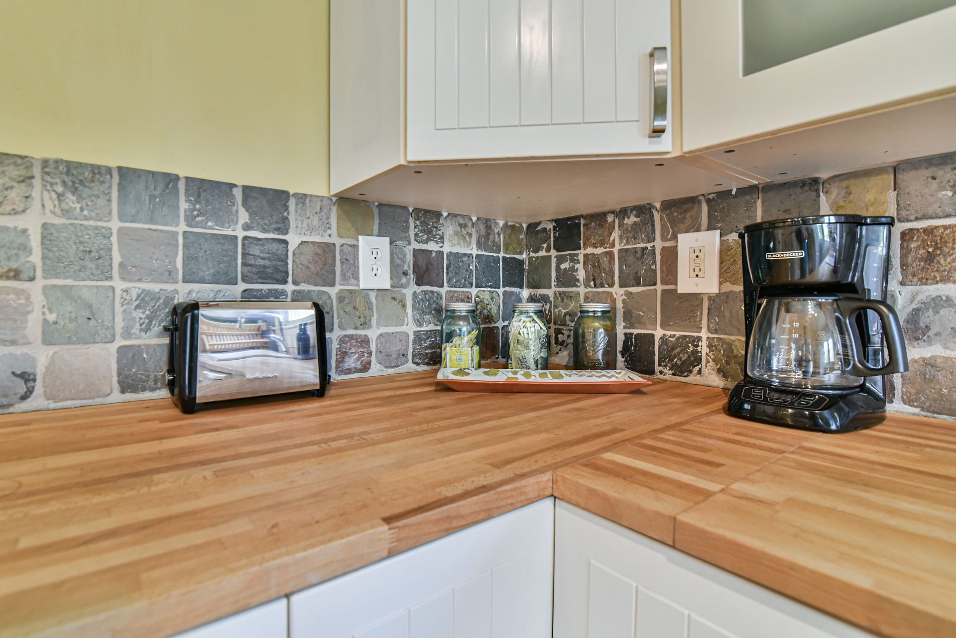 Kitchen corner with wooden countertop, tiled backsplash, toaster, jars, and coffee maker