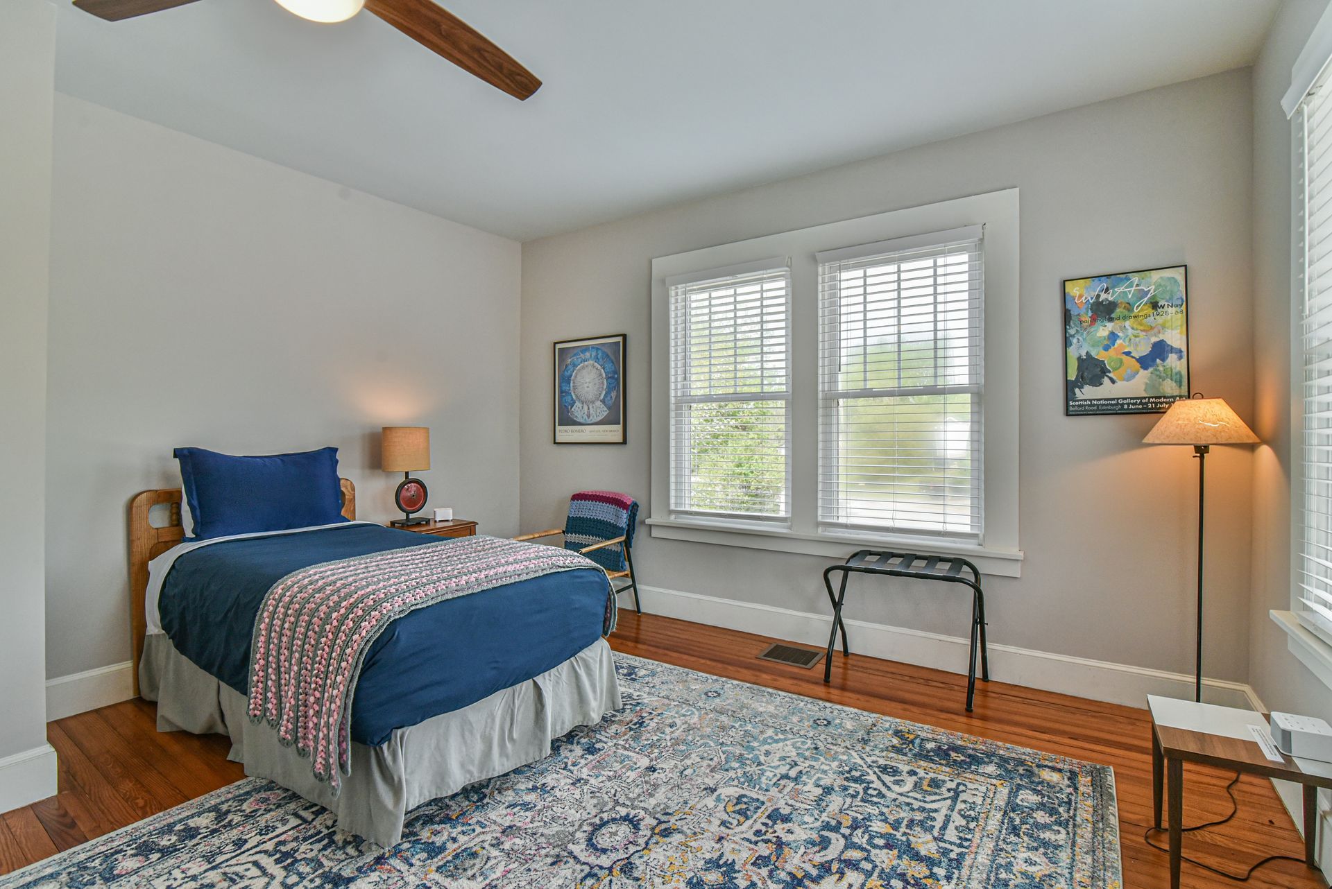 Cozy bedroom with blue bedspread, patterned rug, window bench, and floor lamp