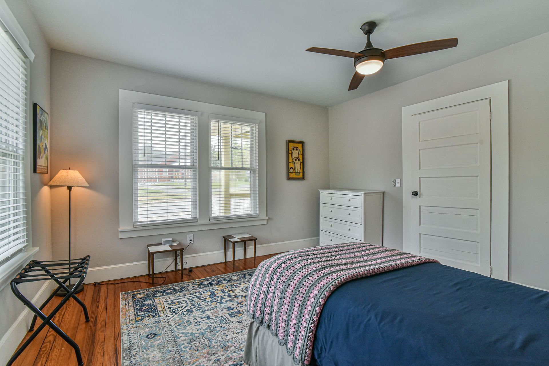 Bedroom with bed, dresser, desk, patterned rug, and window blinds in a light gray room