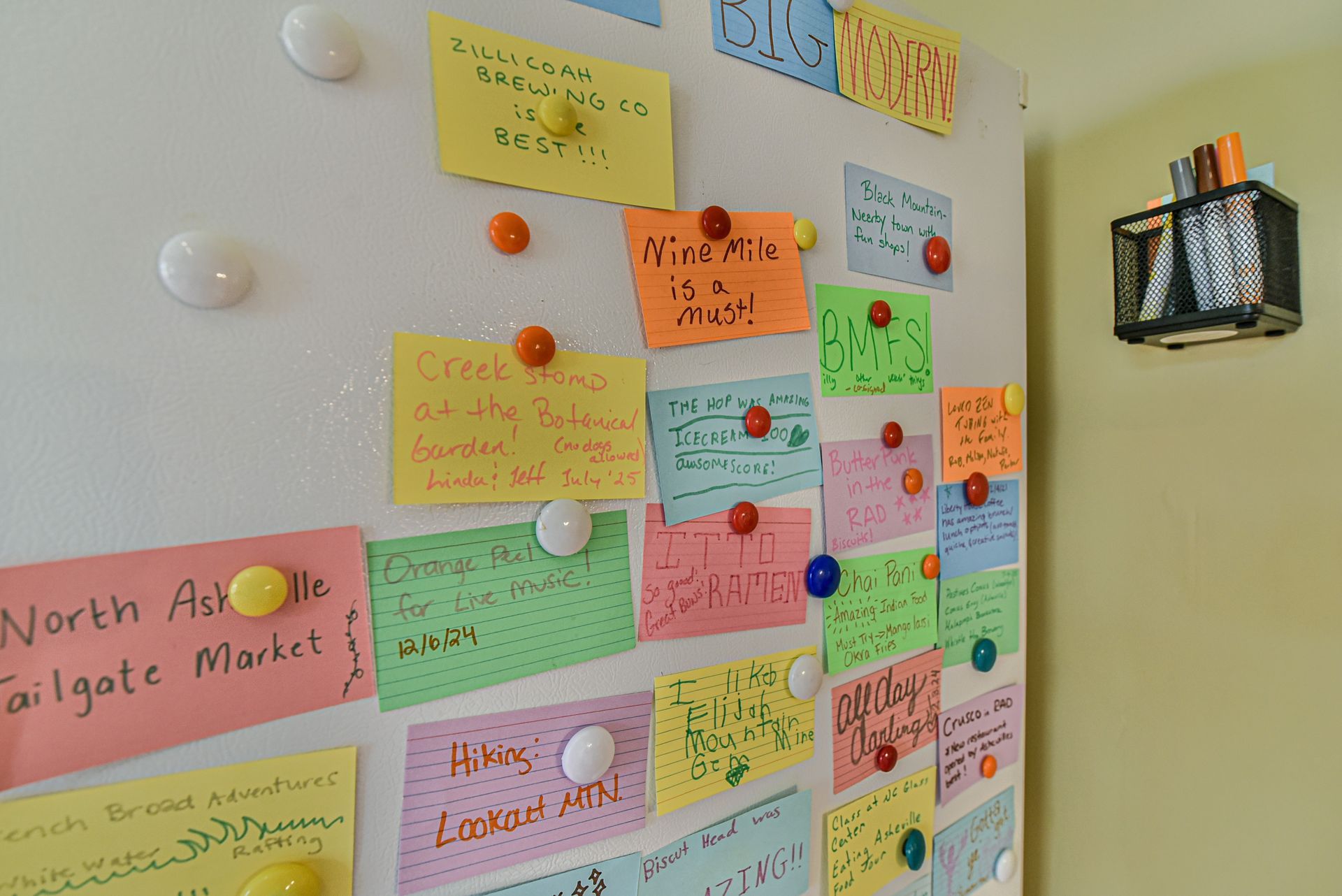 Colorful sticky notes and cards pinned to a wall board, with a few round magnets and a small hanging bin.