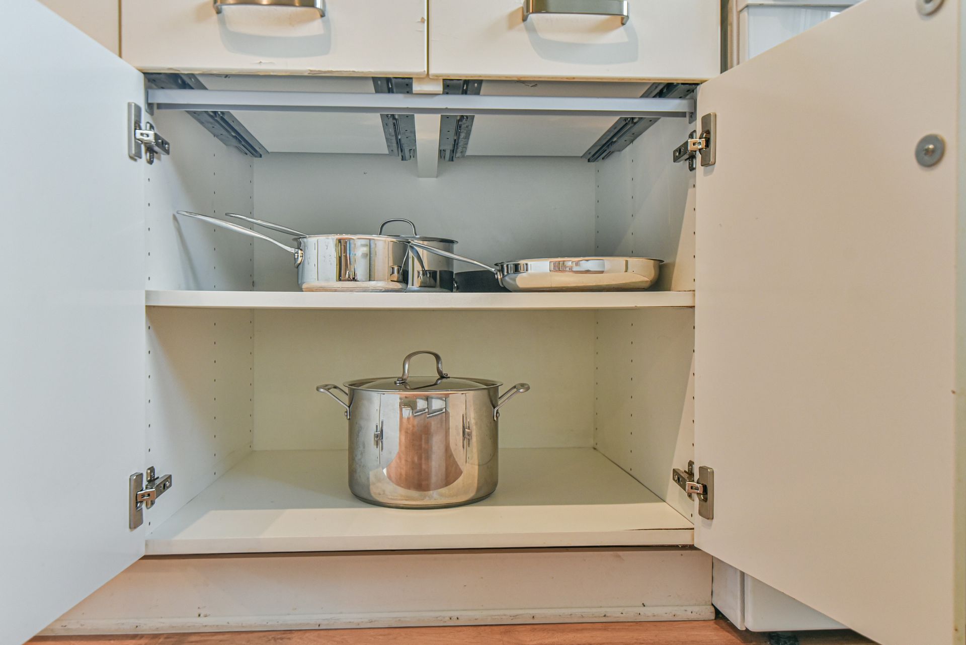 Open kitchen cabinet with pots and pans stored on two shelves