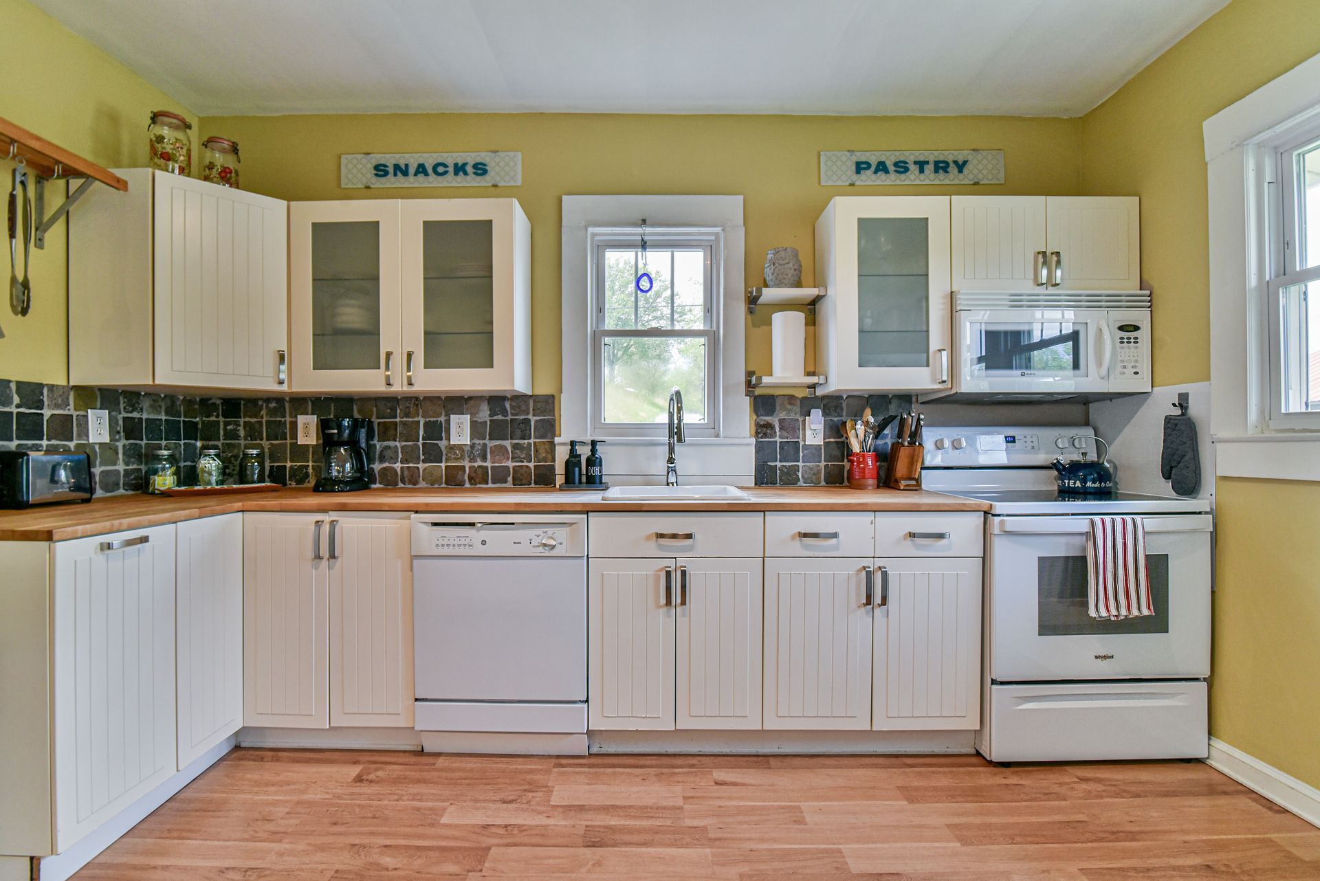 Bright kitchen with white cabinets, green walls, black tile backsplash, and wood floor