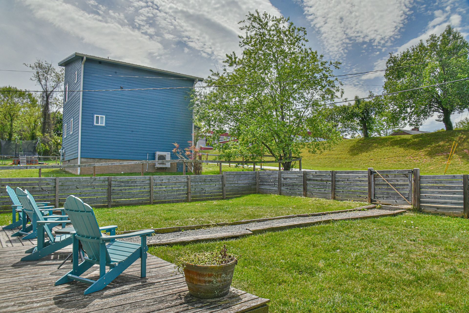 Blue house with fenced lawn, two turquoise chairs, and a tree under a cloudy sky