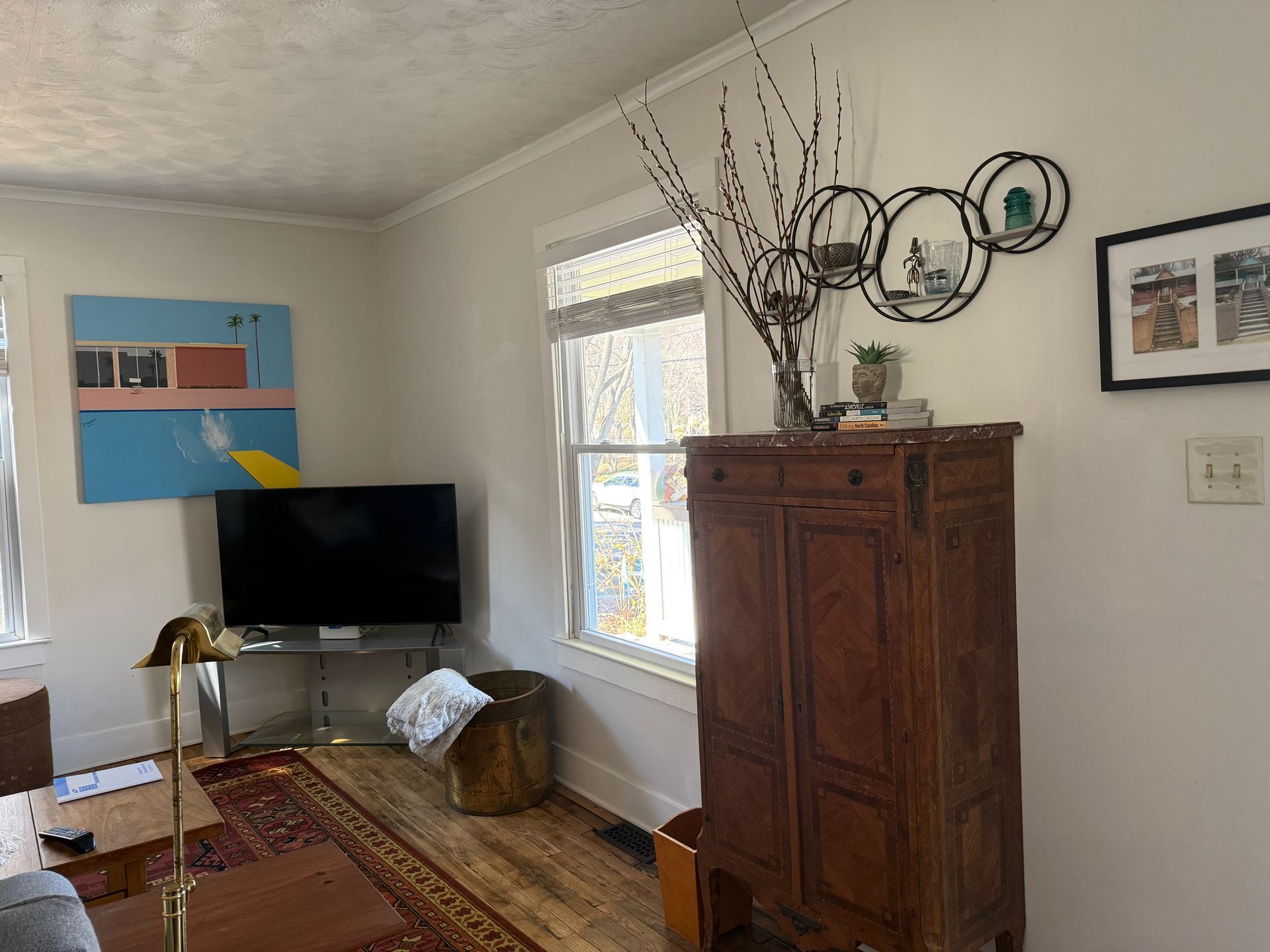 Living room with TV, rug, patterned cabinet, artwork, and a window letting in light