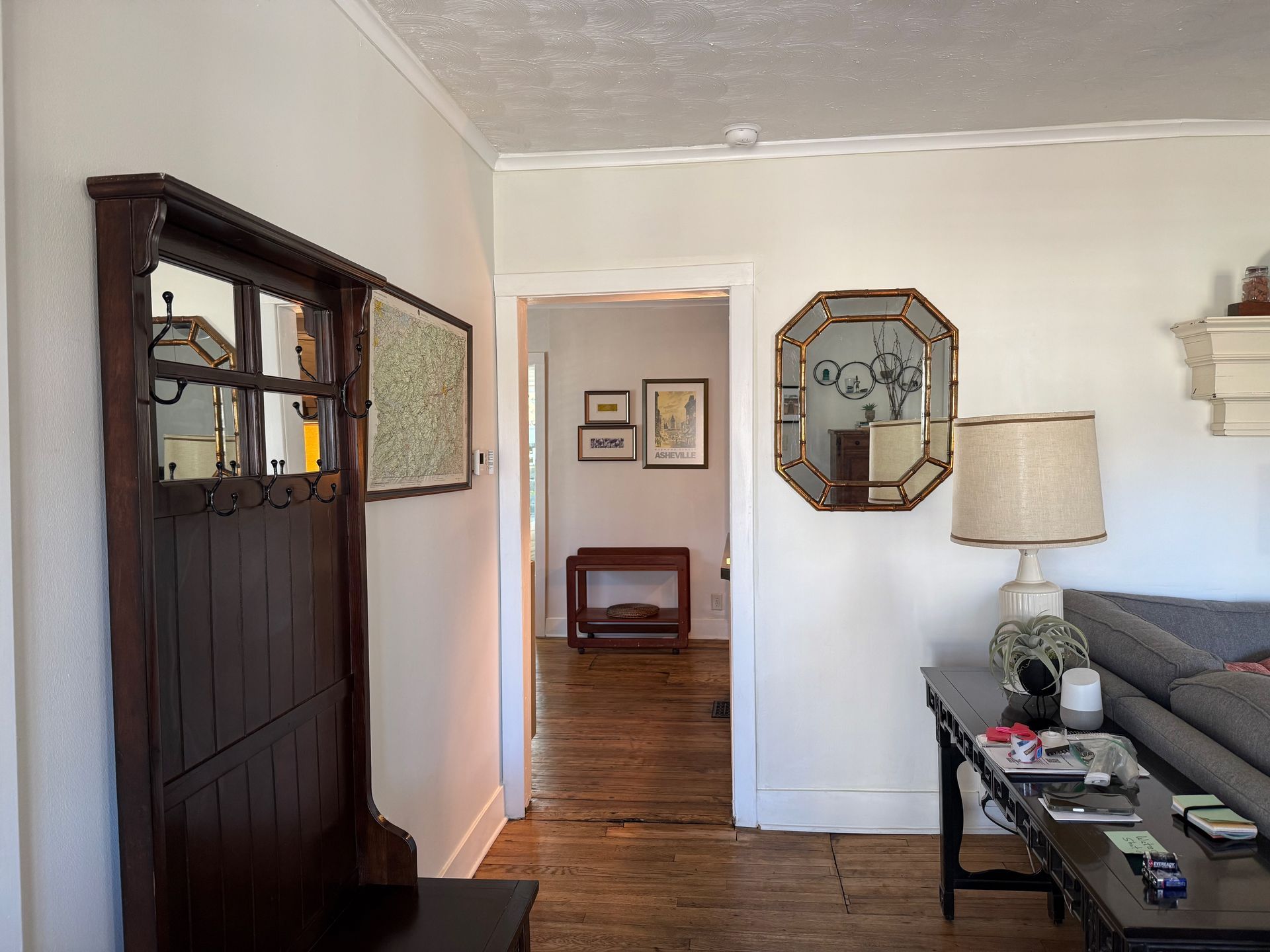Living room with a dark wooden cabinet, gray sofa, lamp, and a doorway to another room with hardwood floors