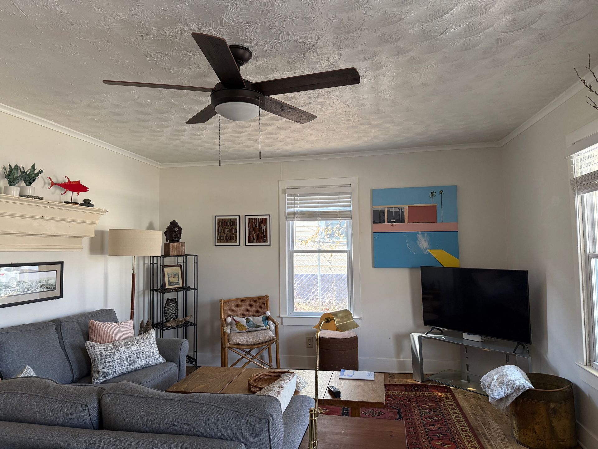 Living room with gray sofa, ceiling fan, TV, wall art, and bright windows