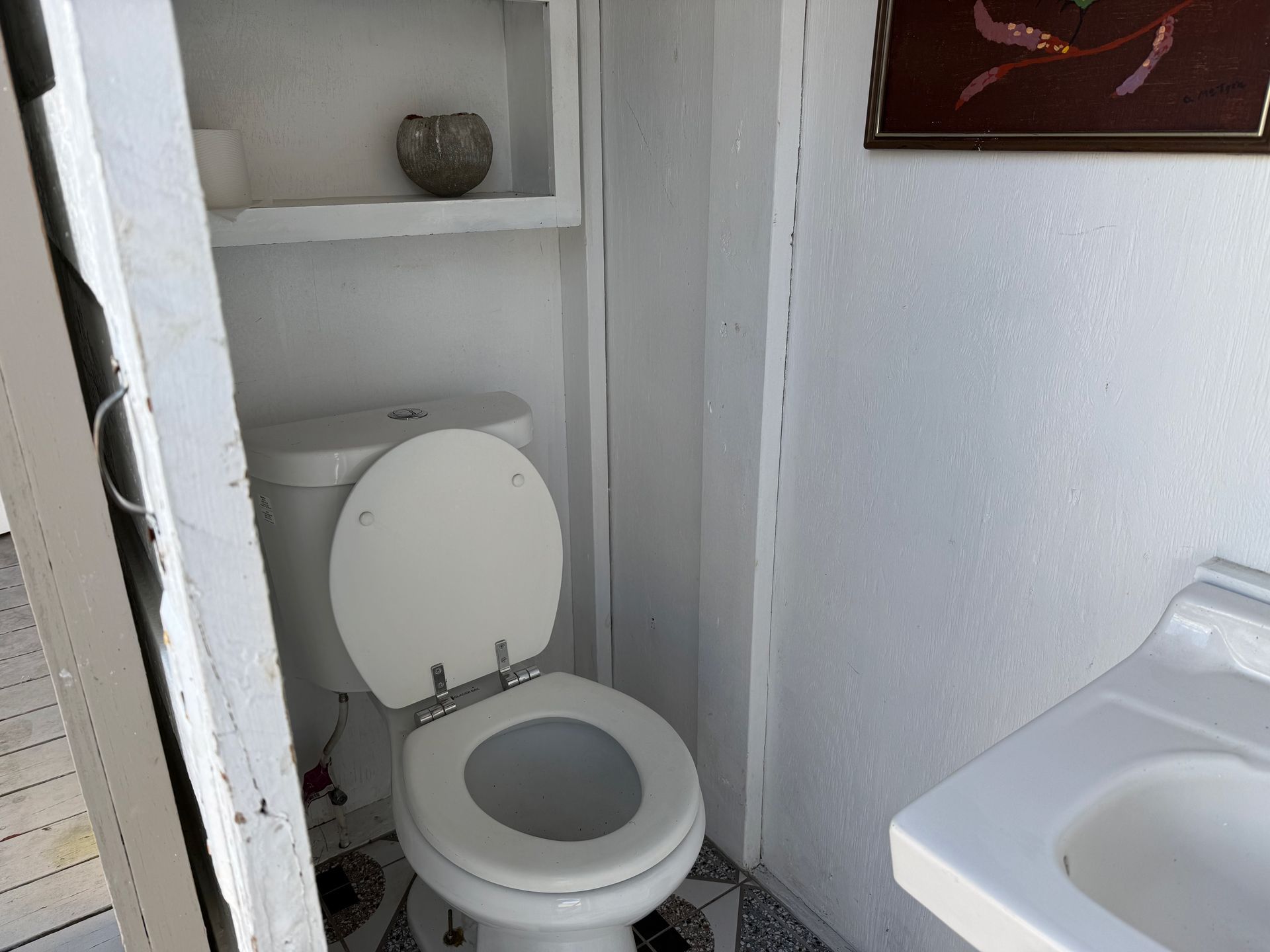 Small bathroom with open toilet, shelf toilet paper, and sink at right.