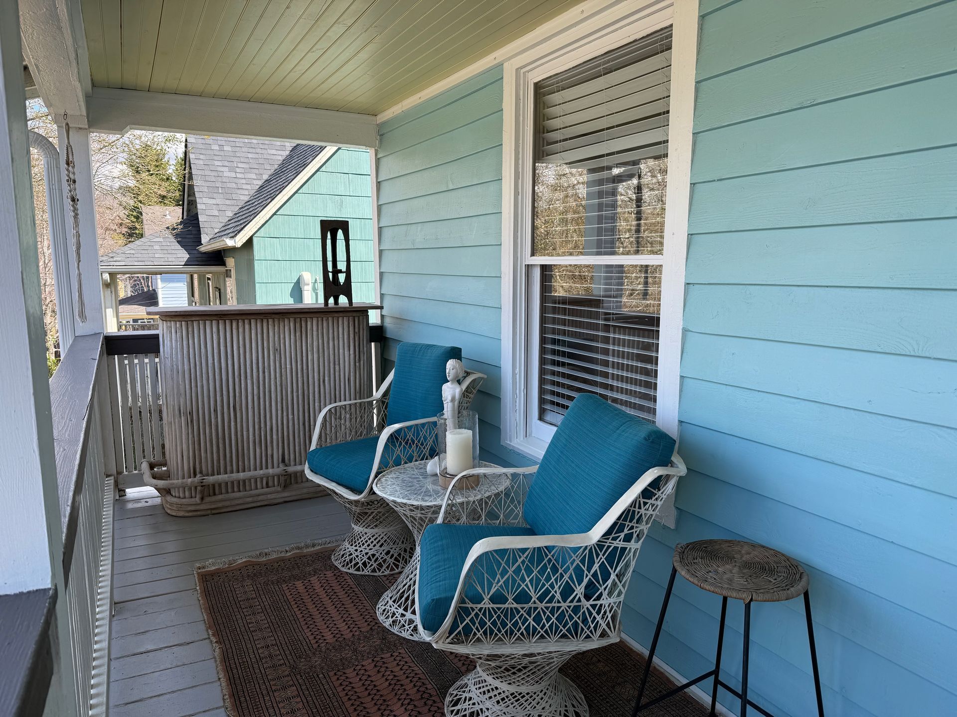 Covered porch with two turquoise chairs, a small table, and a window on light blue siding.