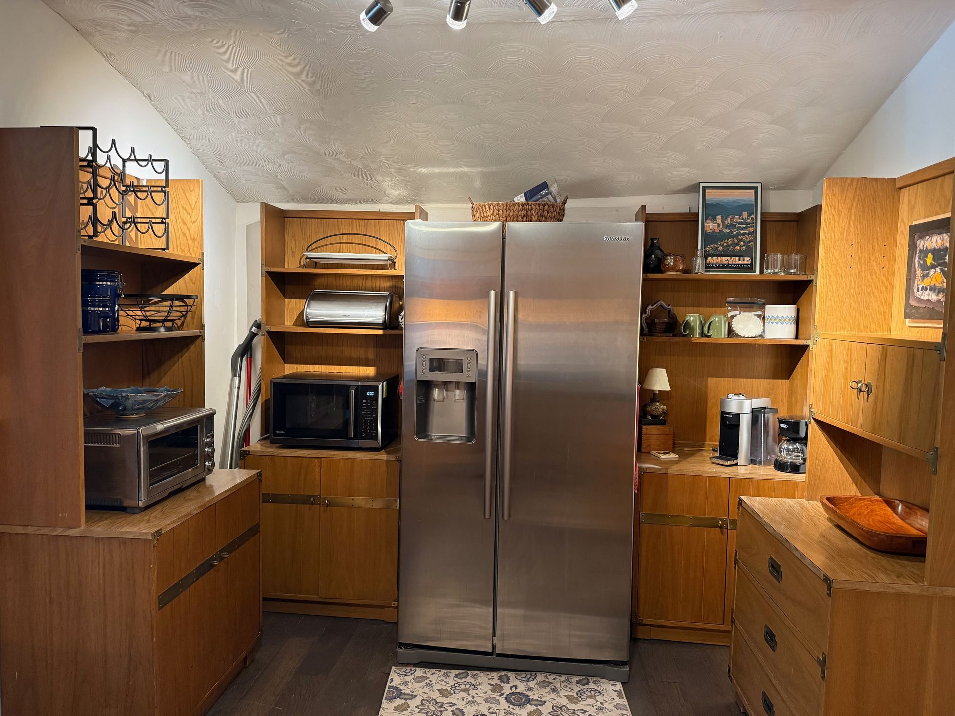 Kitchen with stainless steel refrigerator, wooden cabinets, and countertop appliances on both sides.