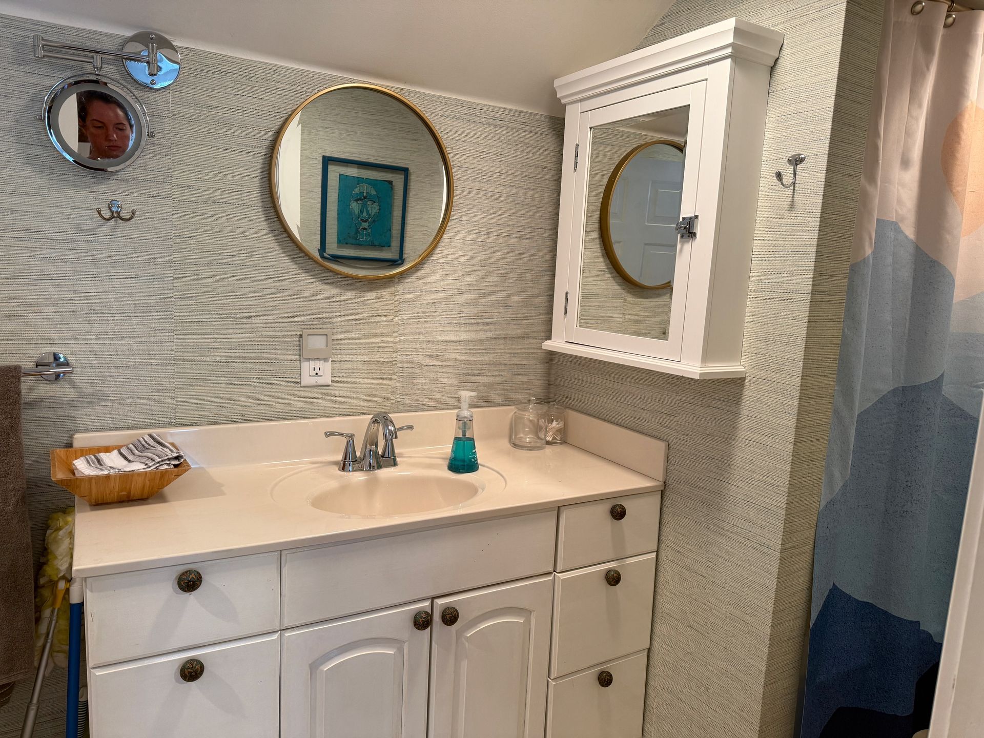 Bathroom vanity with white cabinet, round mirror, wall cabinet, and blue-gray shower curtain