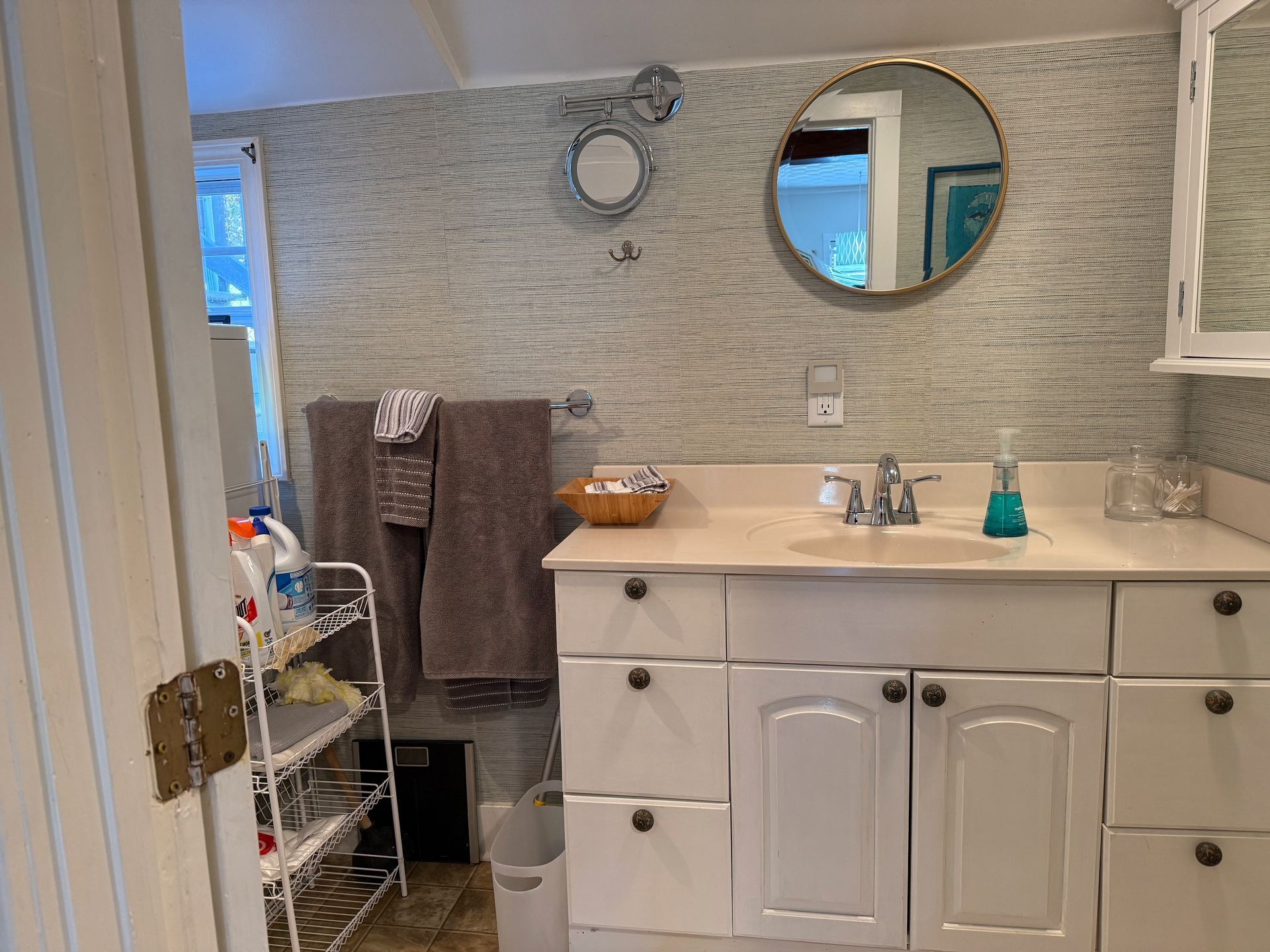 Bathroom with white vanity, round mirrors, gray tiled wall, and towels hanging by an open shower.