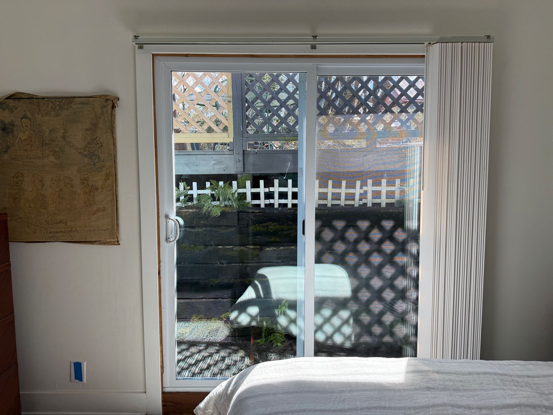 Sliding glass door with white curtain, looking out to a patio and lattice fence