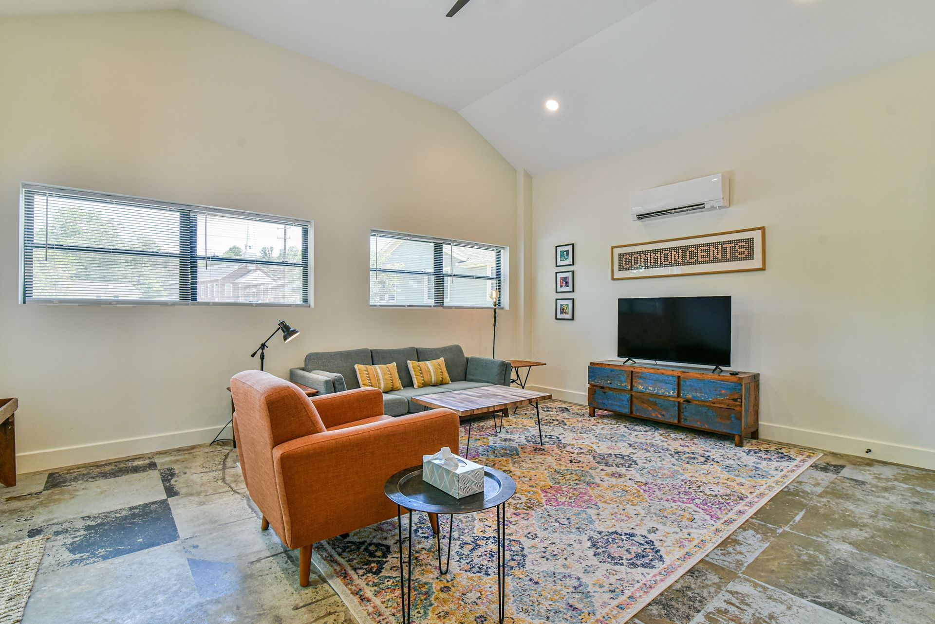 Modern living room with orange chair, gray sofa, TV, patterned rug, and large windows