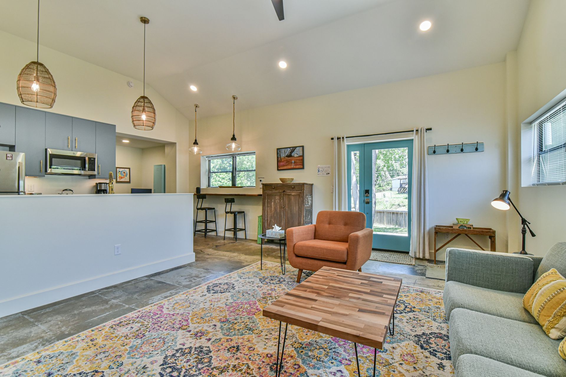 Bright living room with gray sofa, orange chair, patterned rug, and wall art near windows and an open door