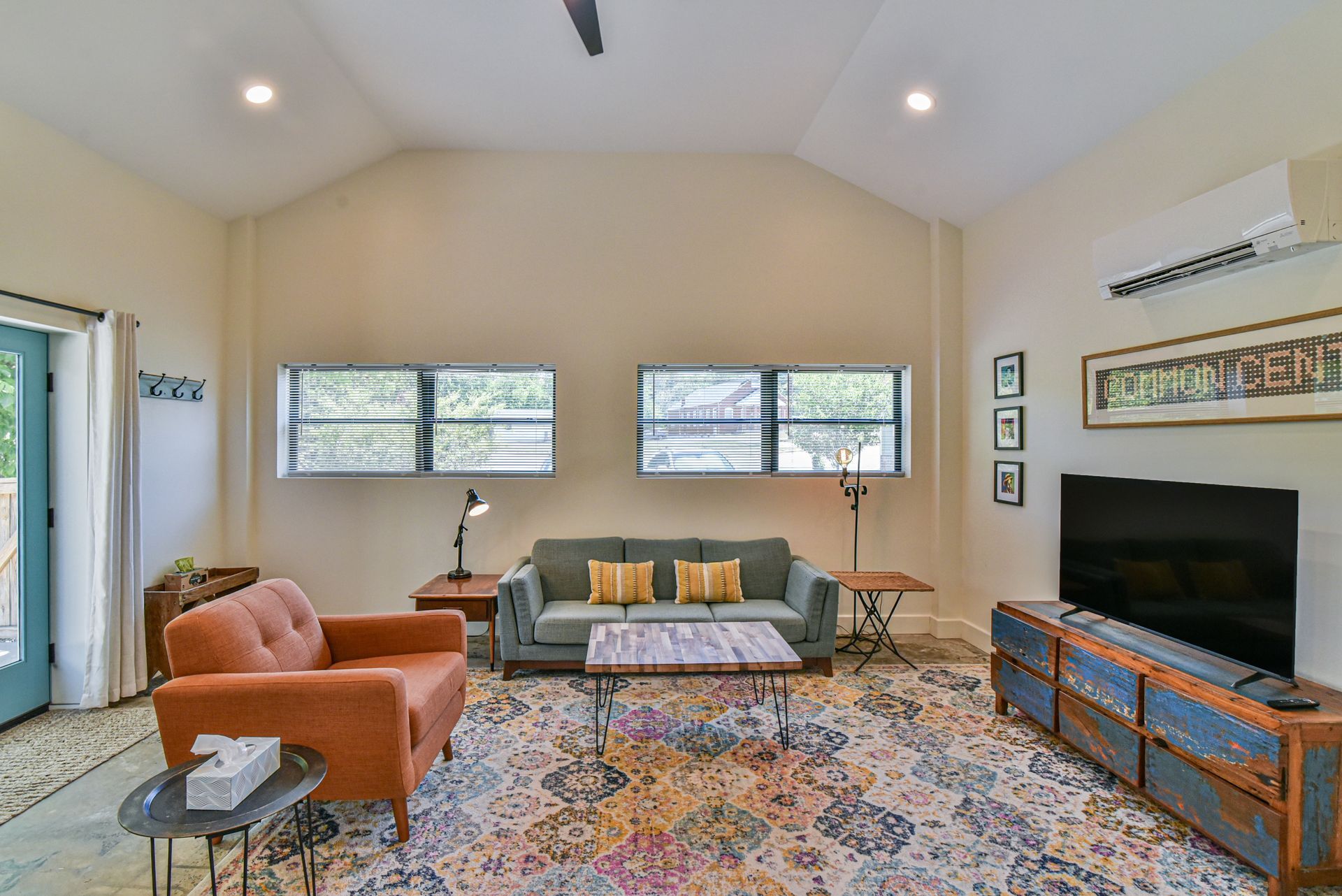 Bright living room with peach chair, gray sofa, patterned rug, TV, and windows under vaulted ceiling