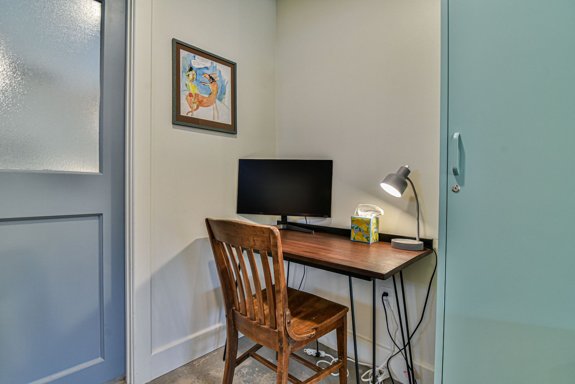 Small home office corner with desk, computer monitor, lamp, and wooden chair near a door