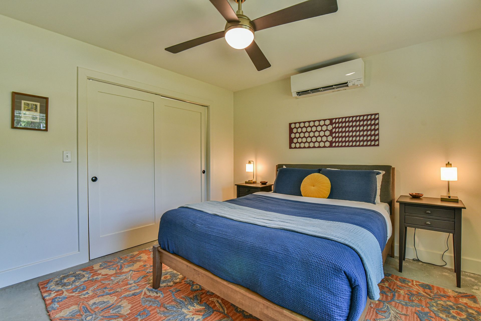 Bedroom with blue bedspread, patterned rug, ceiling fan, and wall-mounted air conditioner