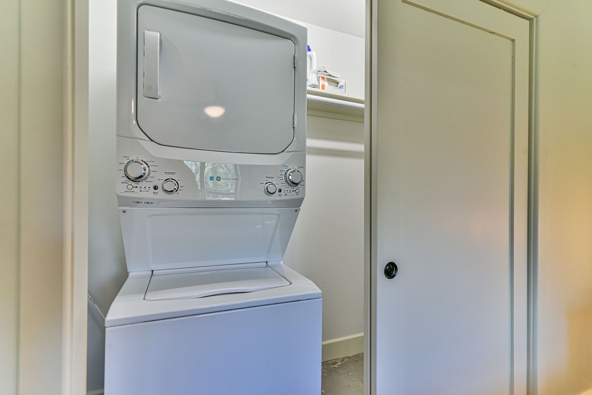 Stacked washer and dryer in a narrow closet with a louvered door nearby.