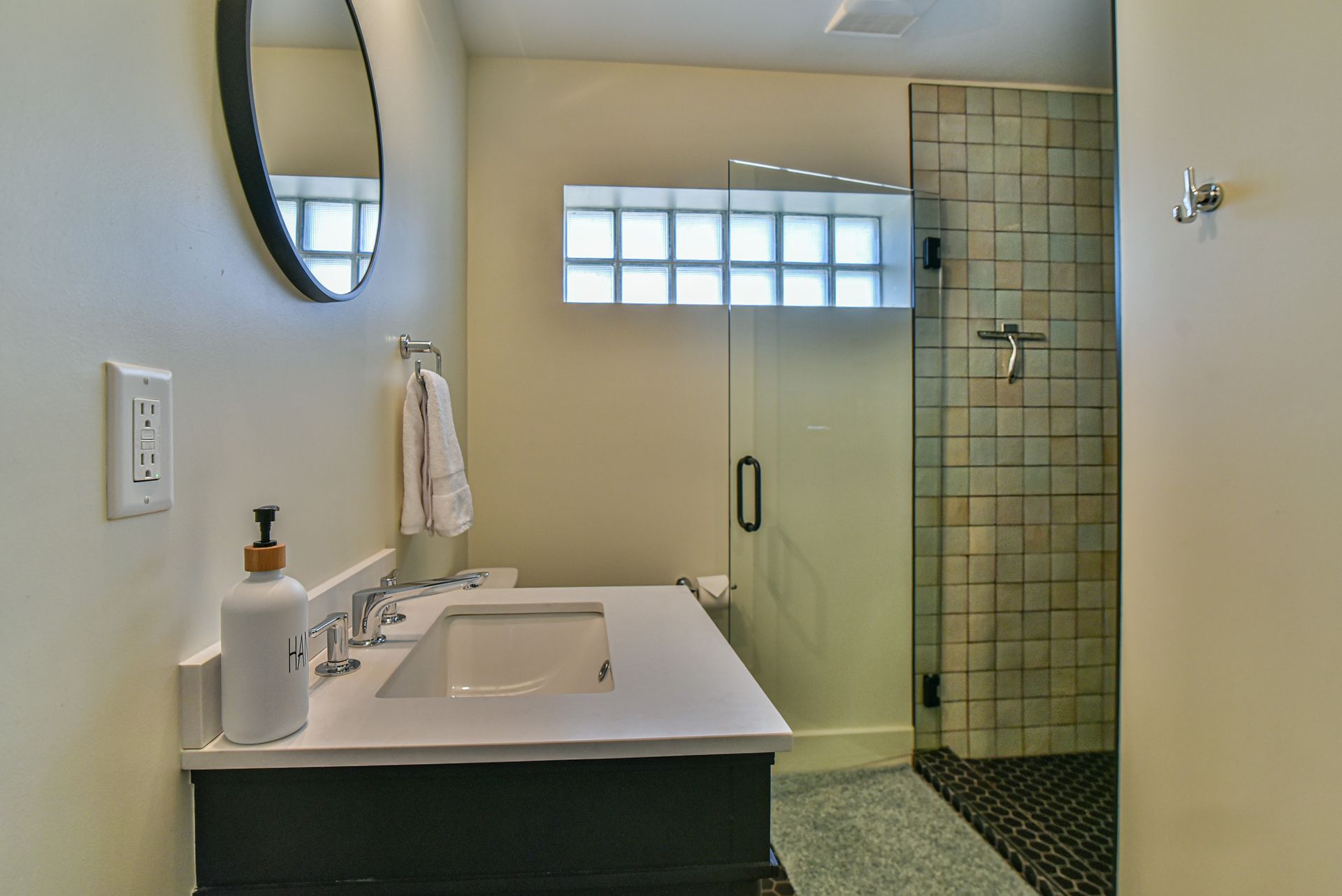 Modern bathroom with vanity, round mirror, window, and tiled walk-in shower