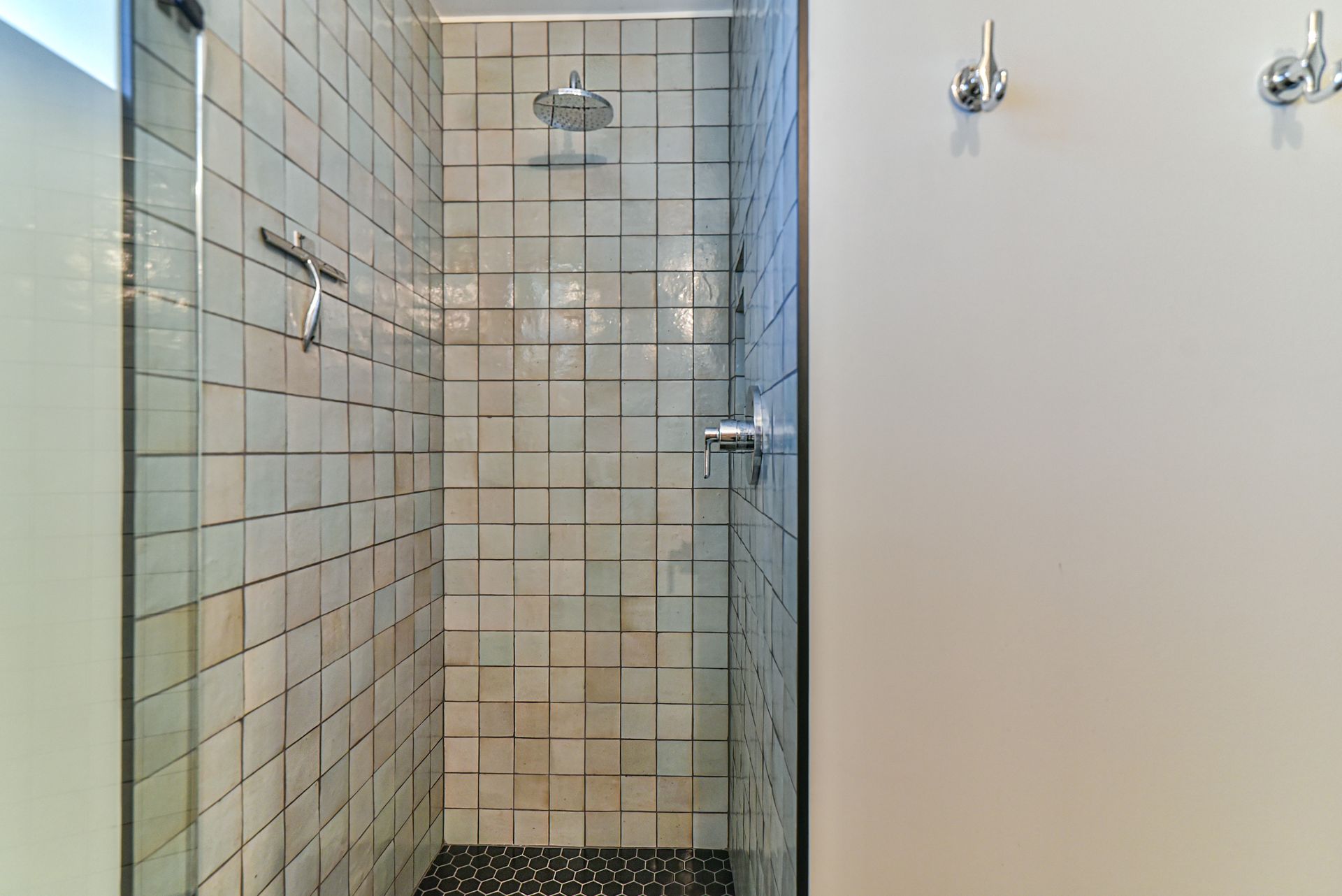 Narrow tiled shower stall with glass door and chrome fixtures in a bathroom