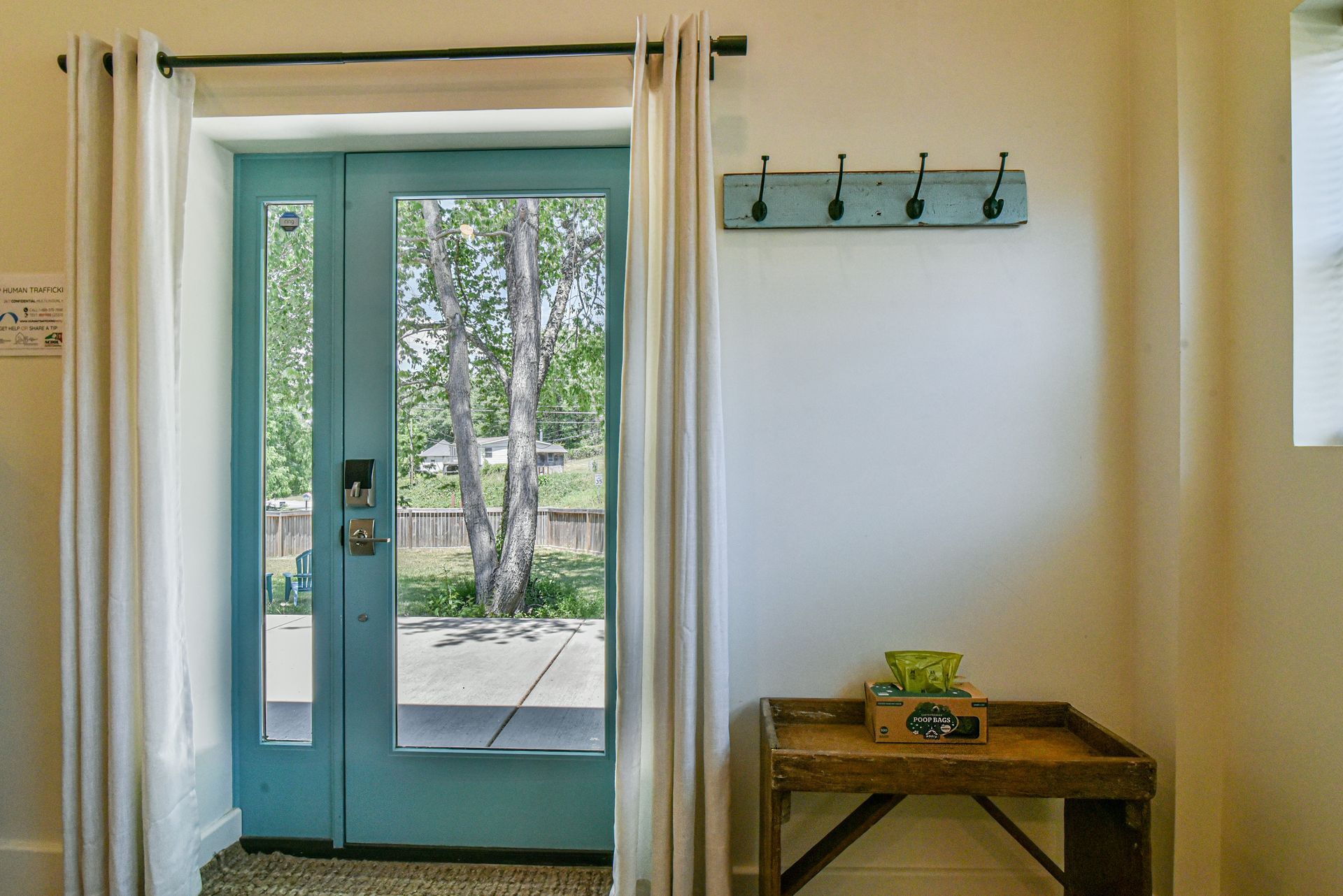 Bright entryway with turquoise front door, white walls, and small wooden table with coat hooks.