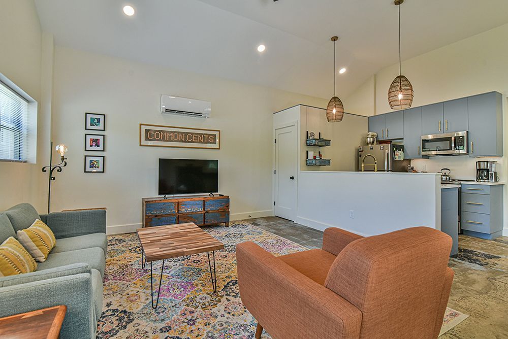 Open-plan living room and kitchen with colorful rug, gray sofa, orange chair, and island seating