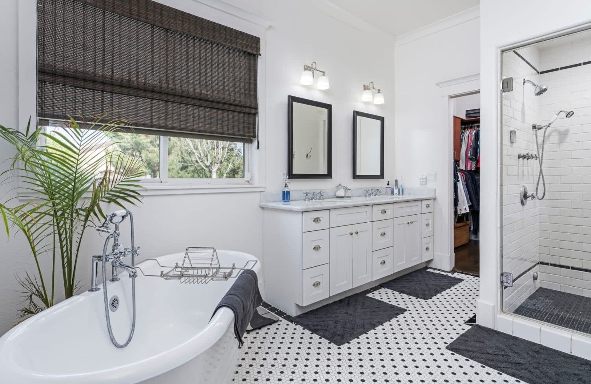 Bright bathroom with white clawfoot tub, black-and-white tile, double vanity, and glass shower.
