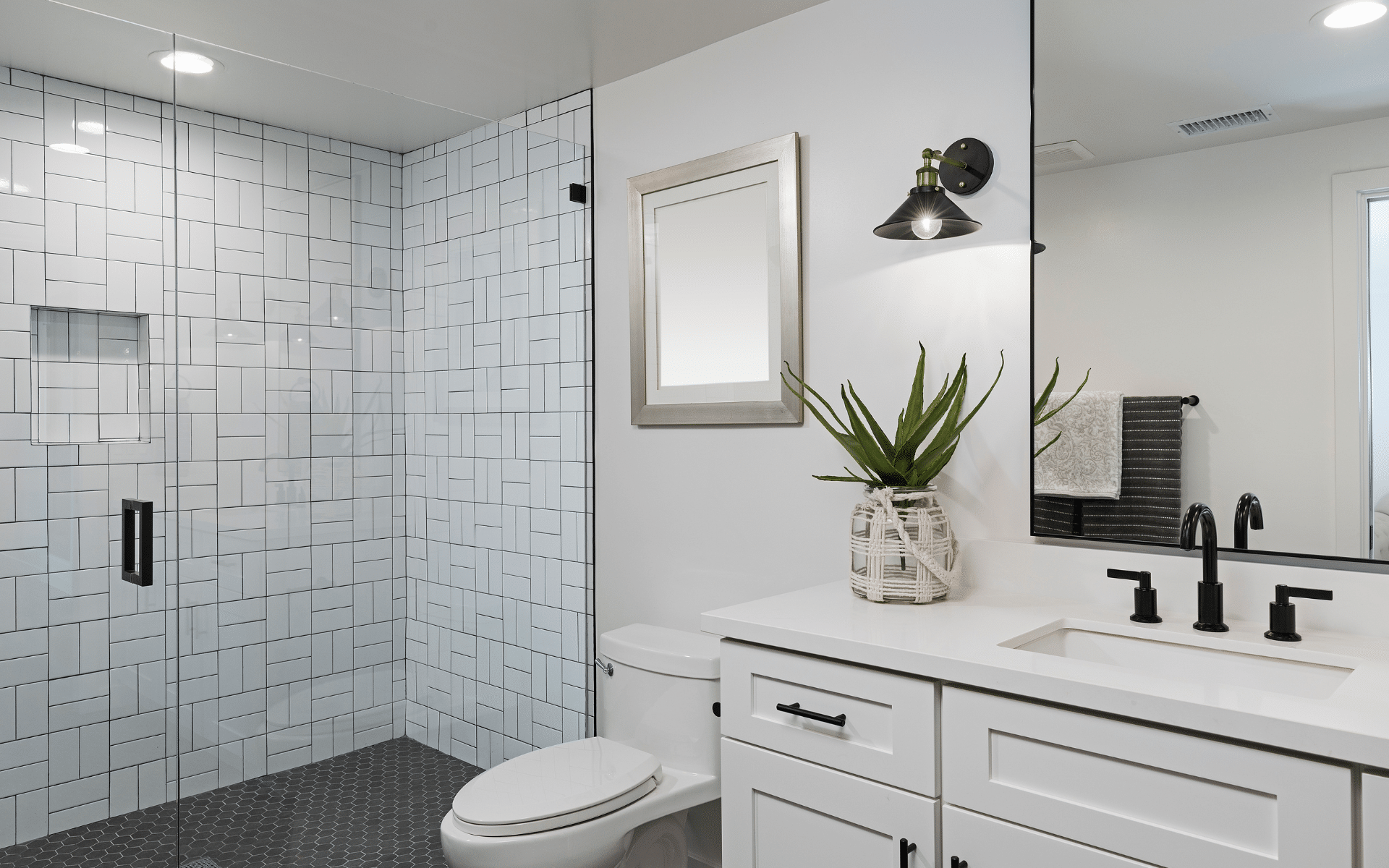 Modern white bathroom with glass shower, toilet, vanity, mirror, and potted plant