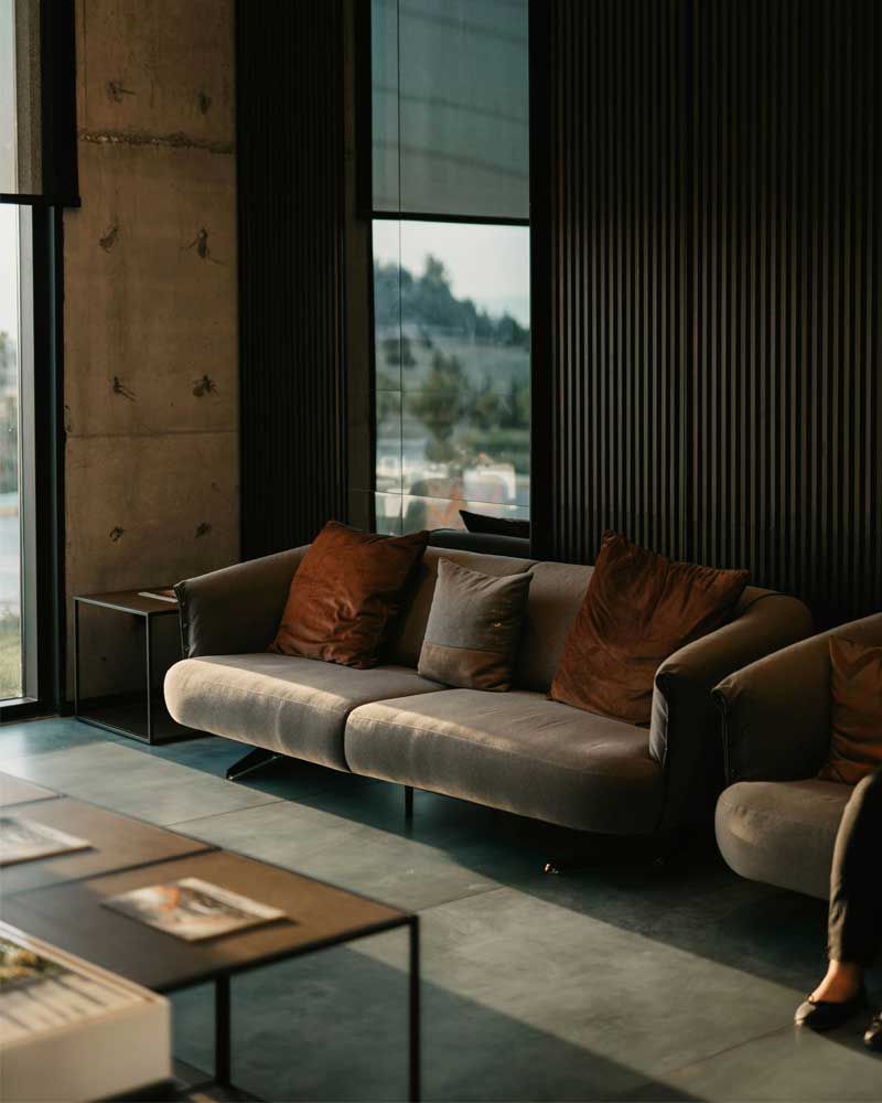 Modern living room with a gray sofa, brown pillows, dark walls, and a large window view