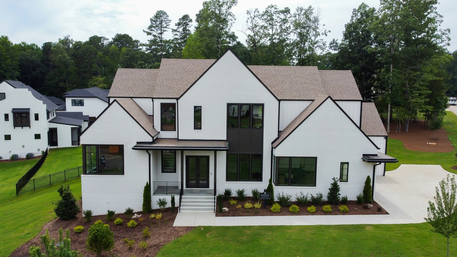Modern white two-story house with black trim, front porch, and landscaped yard surrounded by trees