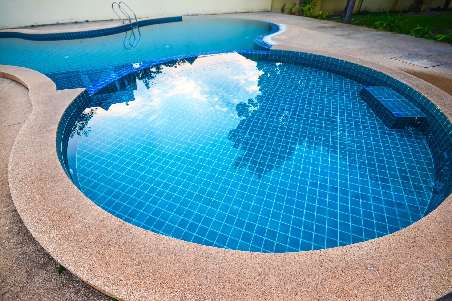 A round blue-tiled swimming pool with a beige deck and clear water reflection