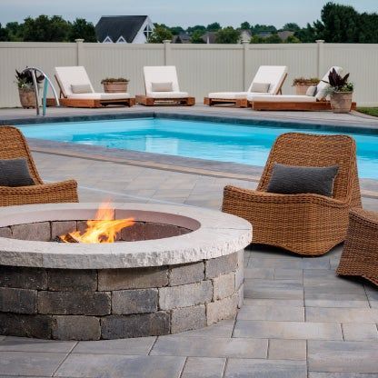 Backyard patio with fire pit, wicker chairs, and a swimming pool at dusk