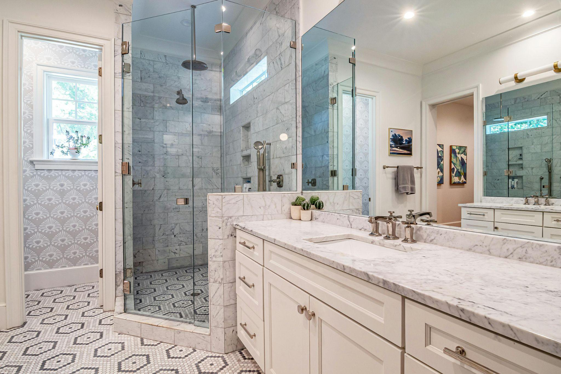 Bright modern bathroom with double vanity, glass shower, marble counters, and patterned tile floor