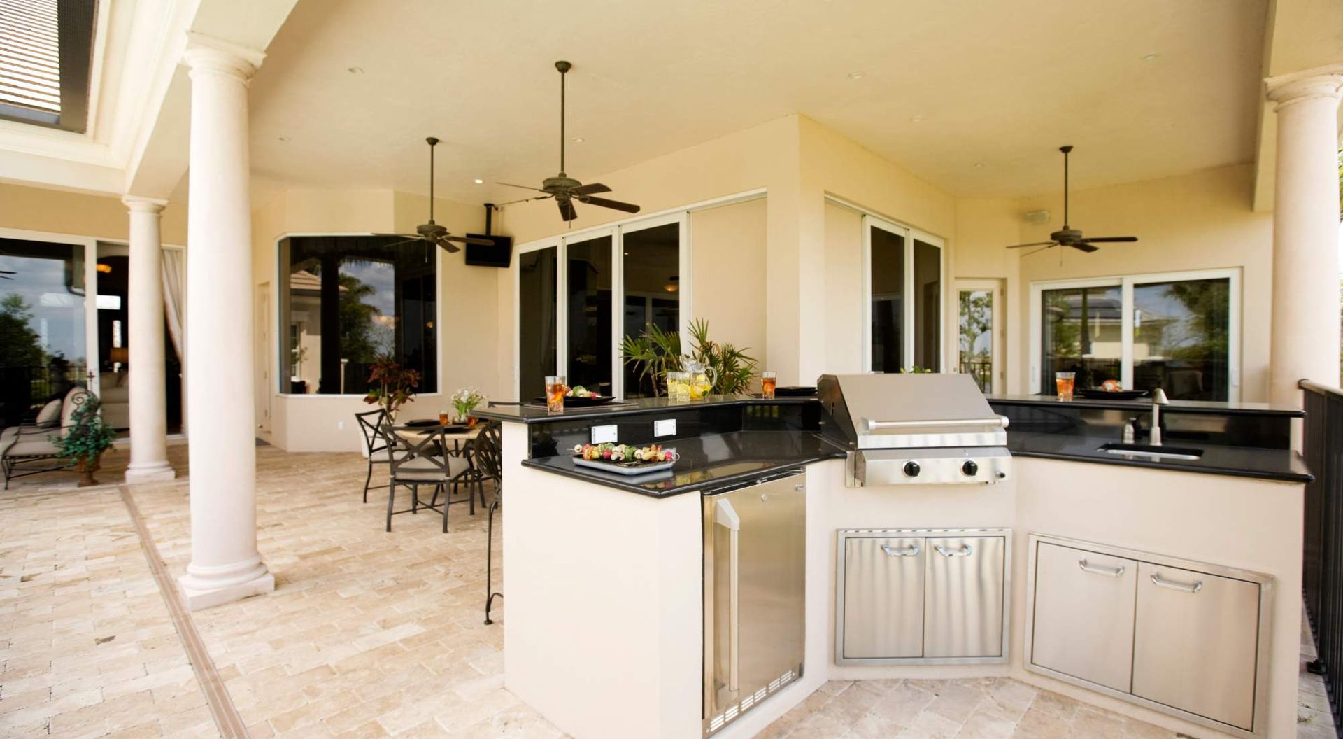 Covered patio with outdoor kitchen, grill, bar seating, and ceiling fans overlooking a poolside area