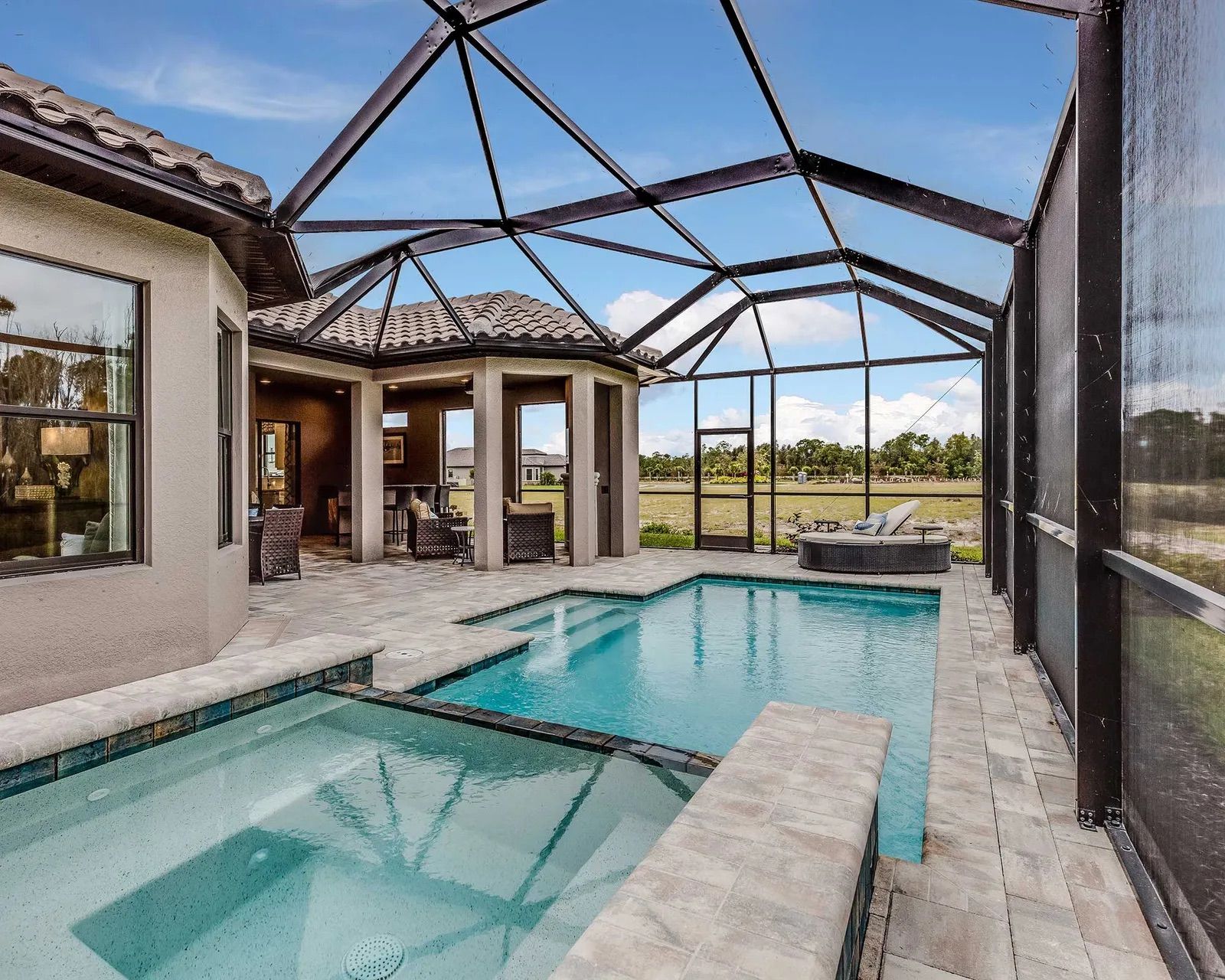 Screened backyard pool and spa beside a house with patio and open view beyond