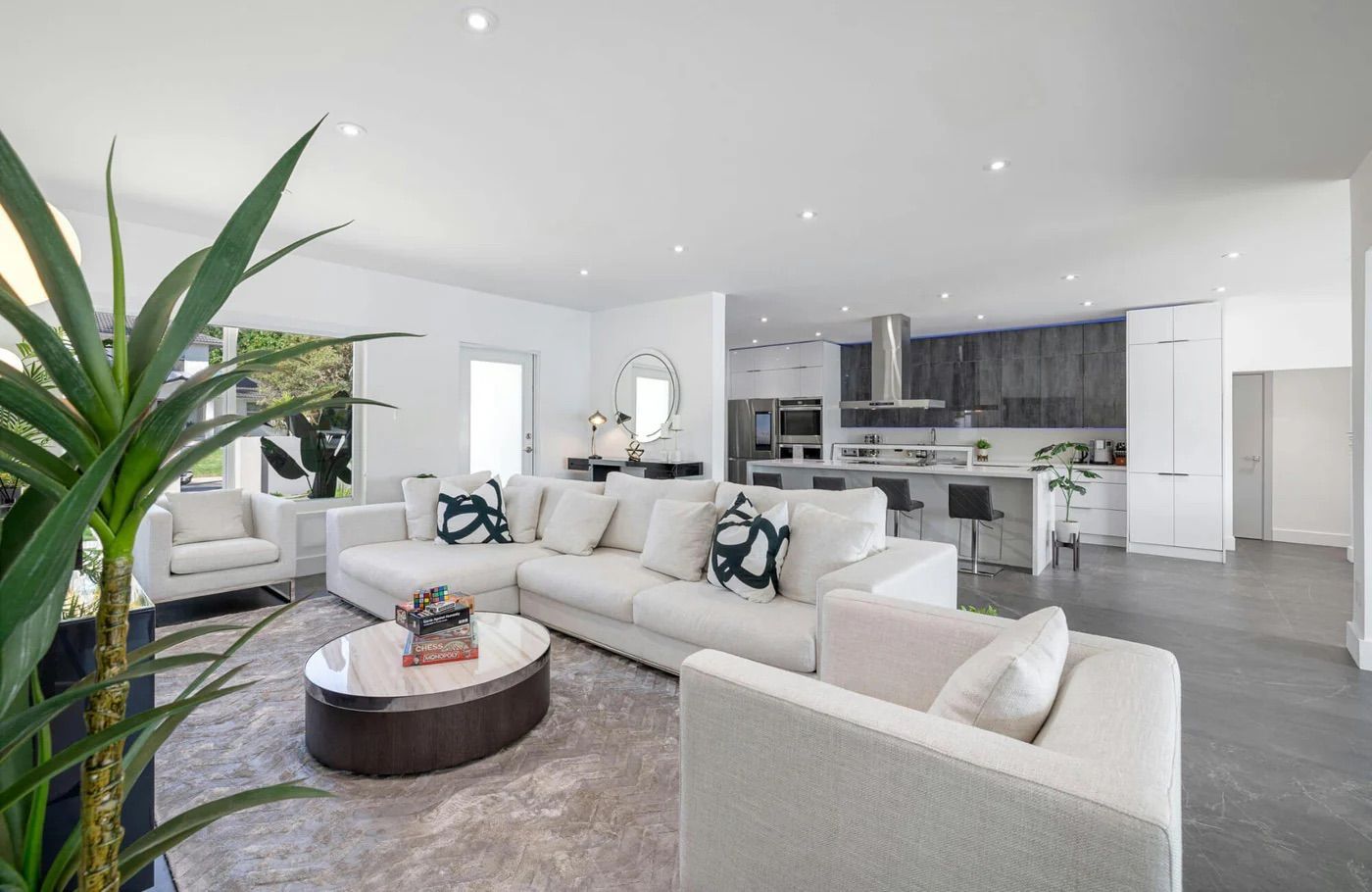 Bright modern open-plan living room and kitchen with white sofas, gray floors, and a round coffee table