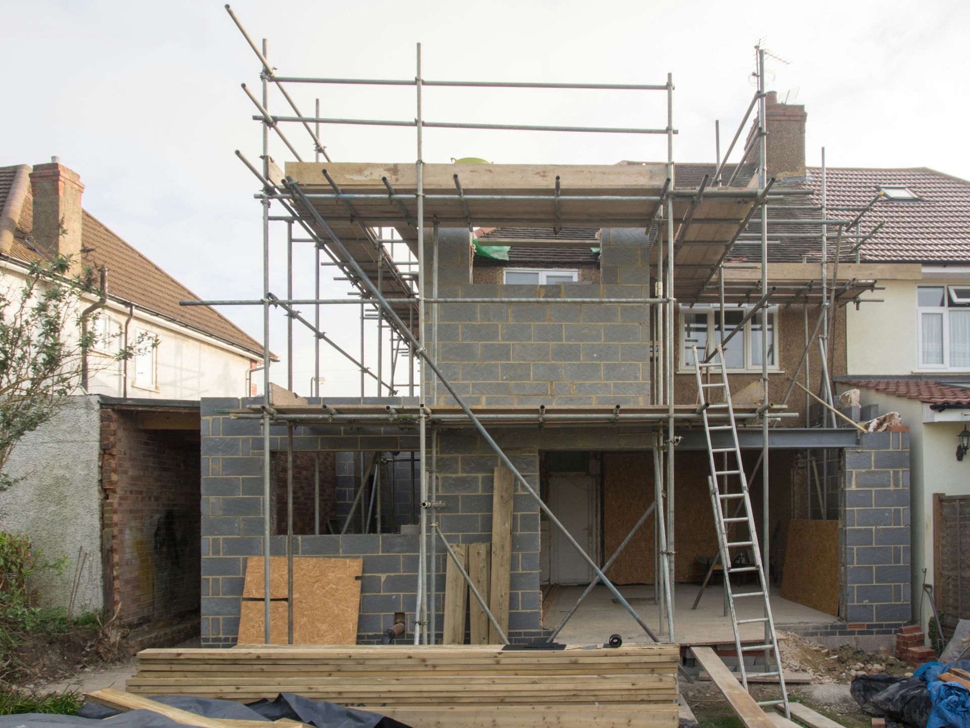 House under construction with scaffolding, exposed brick walls, and a ladder at the front.