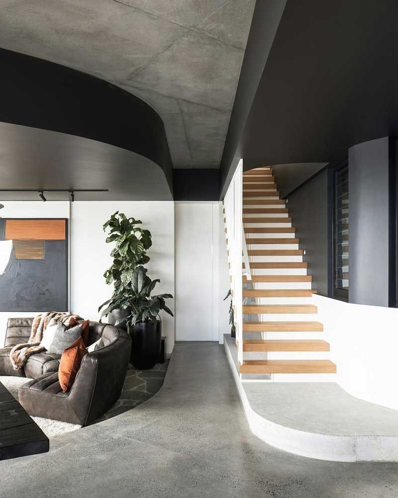 Modern living room with curved sofa, tall plant, and open staircase with wood steps and black walls