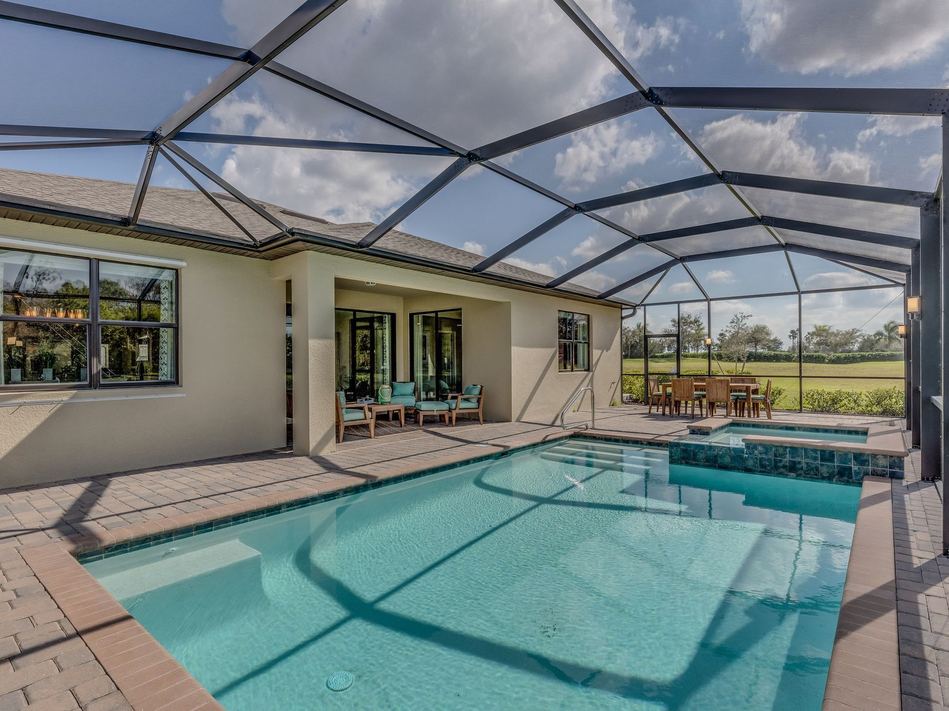Covered backyard pool with screened enclosure beside a patio and house, overlooking open fields