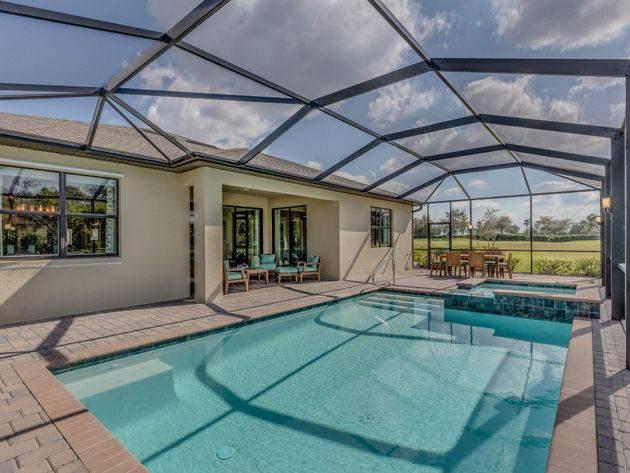 Screened backyard pool with patio seating beside a modern house under a metal canopy