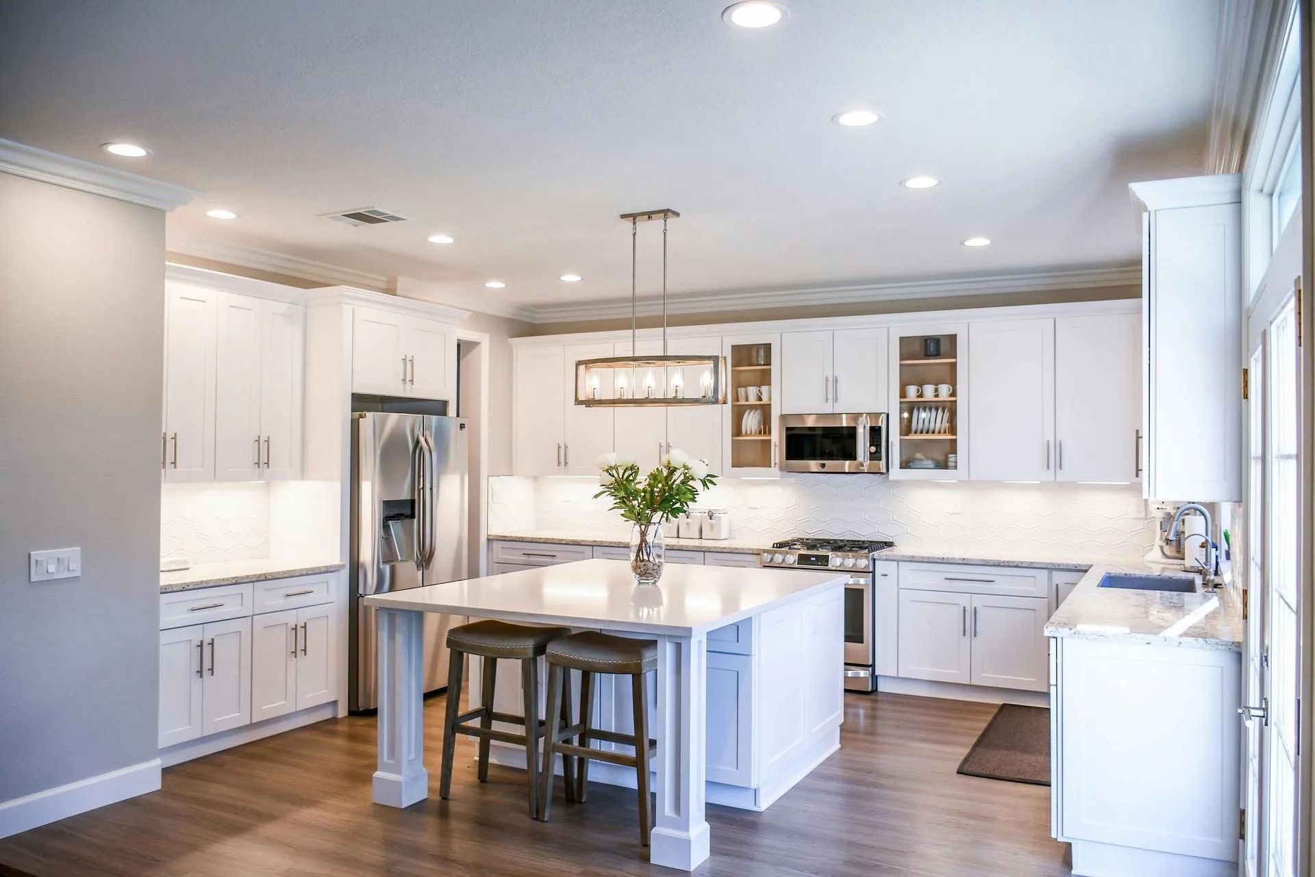Bright modern kitchen with white cabinets, island, stainless steel appliances, and wood floors