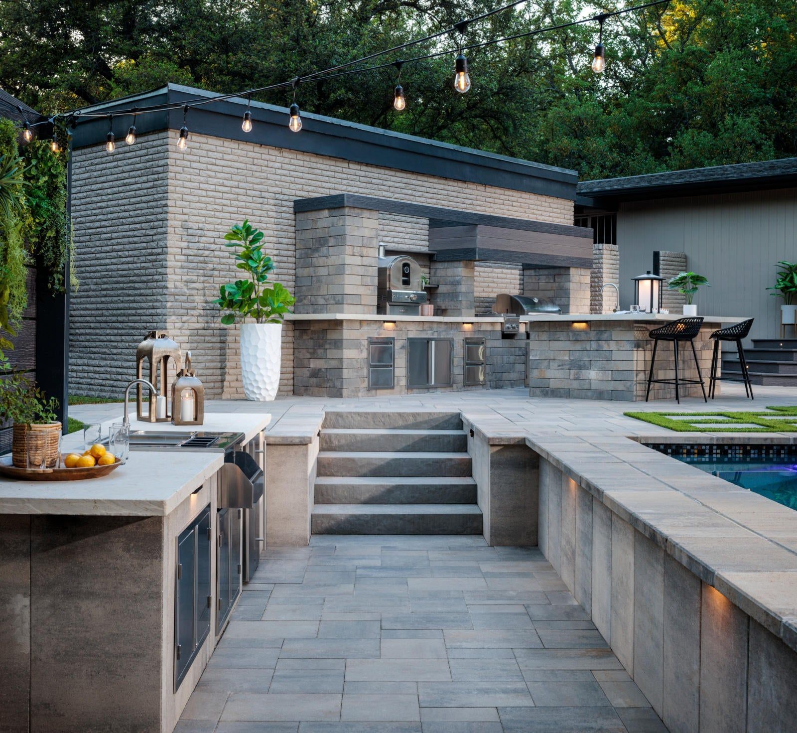 Modern outdoor kitchen and patio with stone steps, built-in grill, and poolside seating area