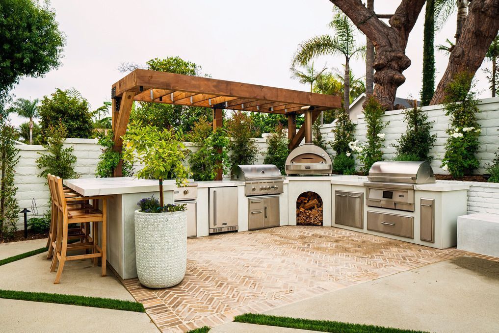 Outdoor backyard kitchen with stone grill, white cabinets, and pergola amid lush greenery