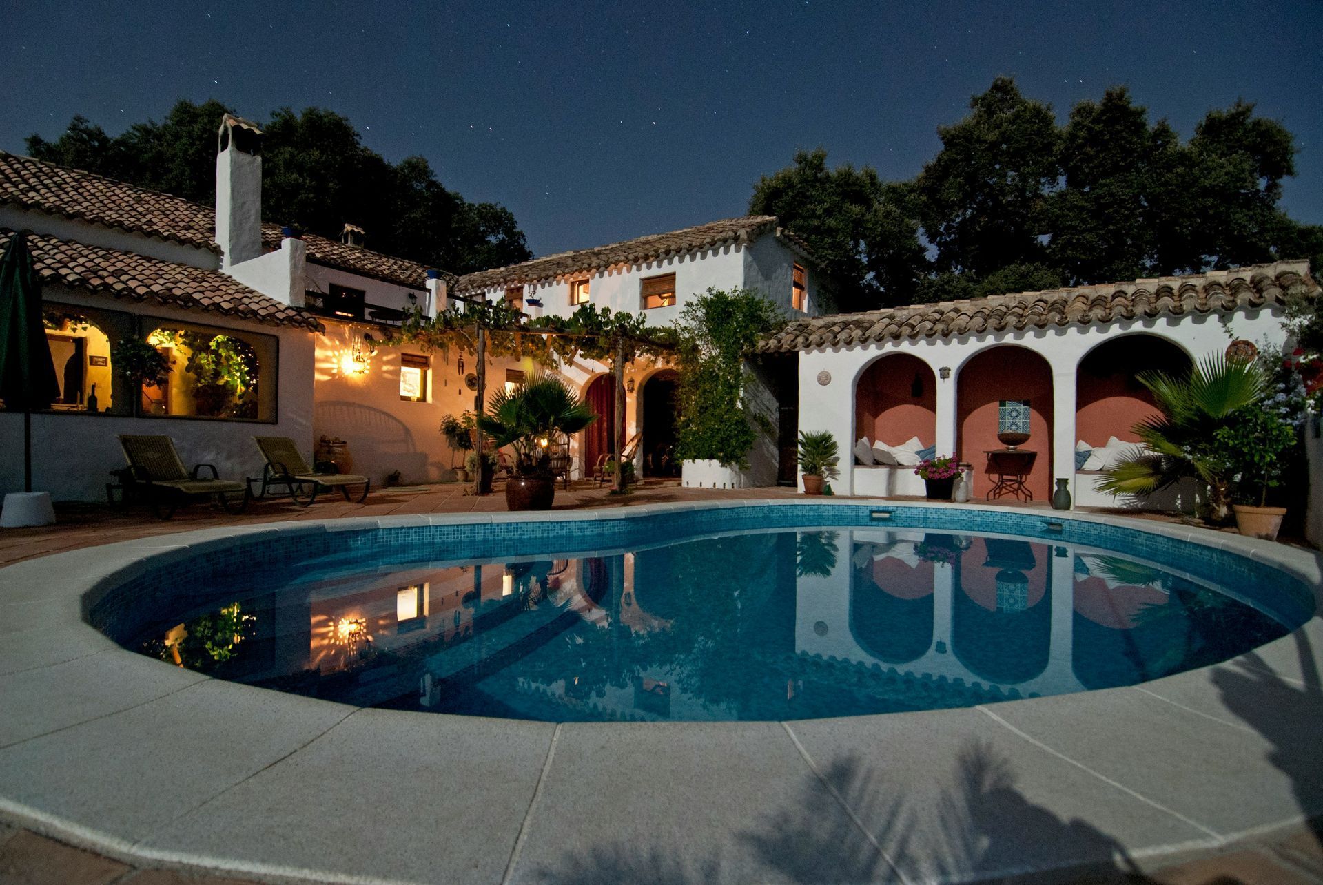 Courtyard villa with a lit swimming pool at dusk, arched verandas, and warm yellow lights