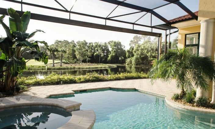Covered backyard pool with turquoise water, patio seating, and lush greenery overlooking a lake