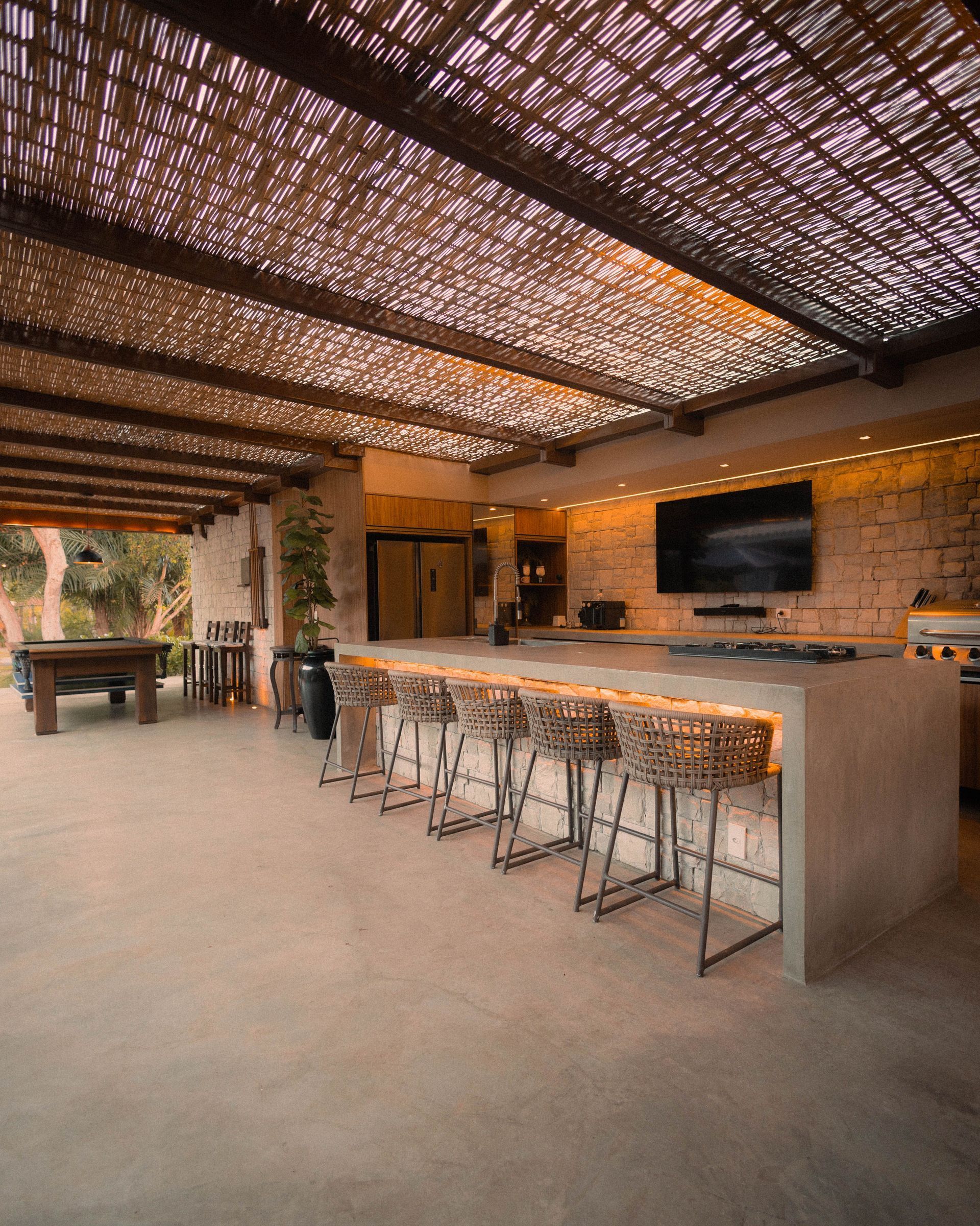 Open-air stone patio bar with woven ceiling, bar stools, and pool table