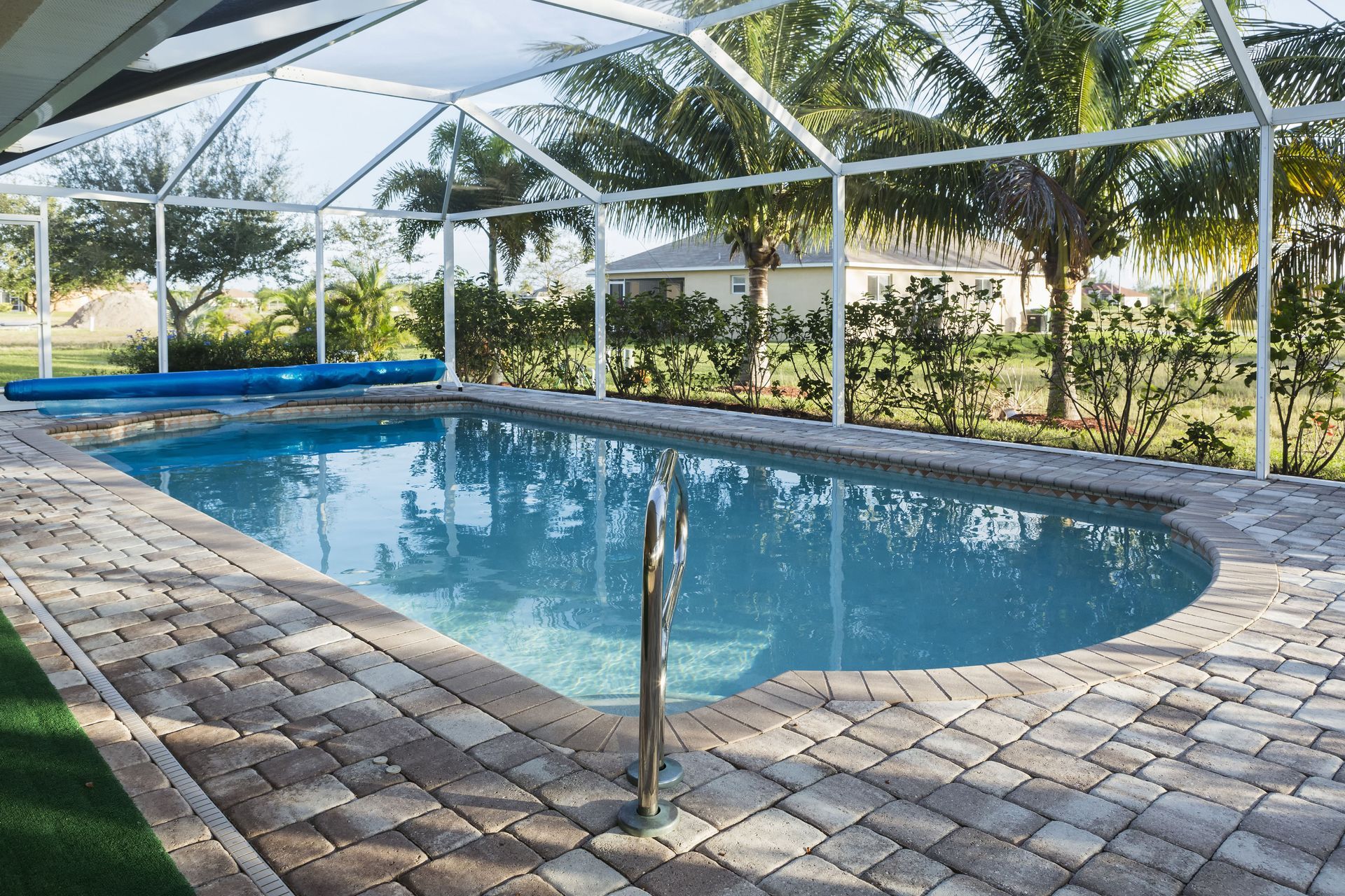 Covered outdoor pool with clear blue water, stone deck, and screened enclosure surrounded by palm trees